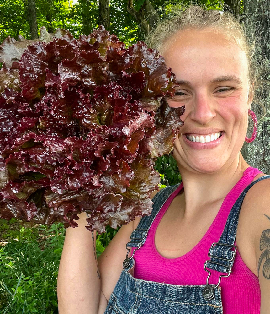 Emma smiles at the camera, holding a bunch of lettuce