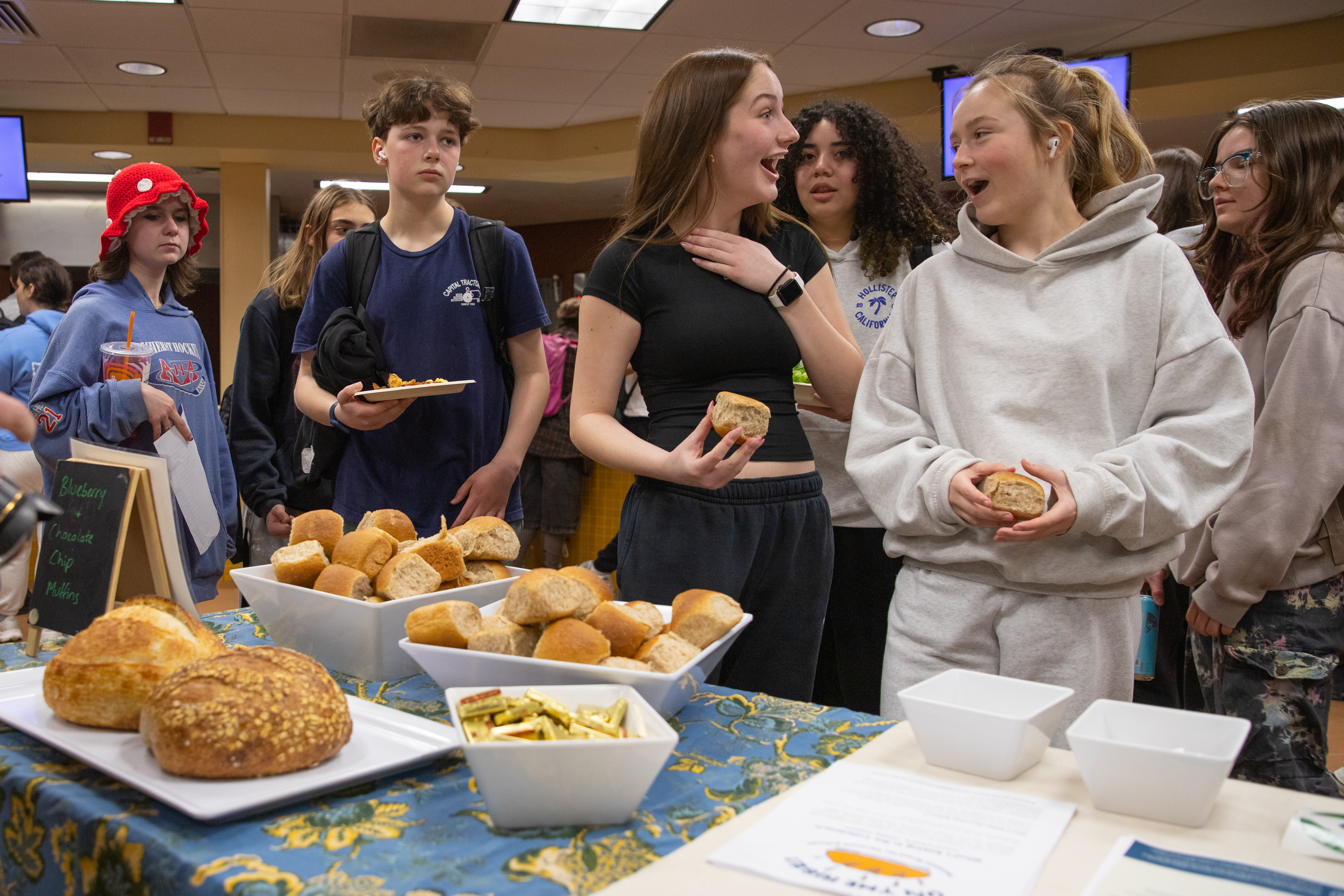 students appear enthusiastic to sample the new local rolls offered in their cafeteria as they stand before a table filled with samples of the rolls.