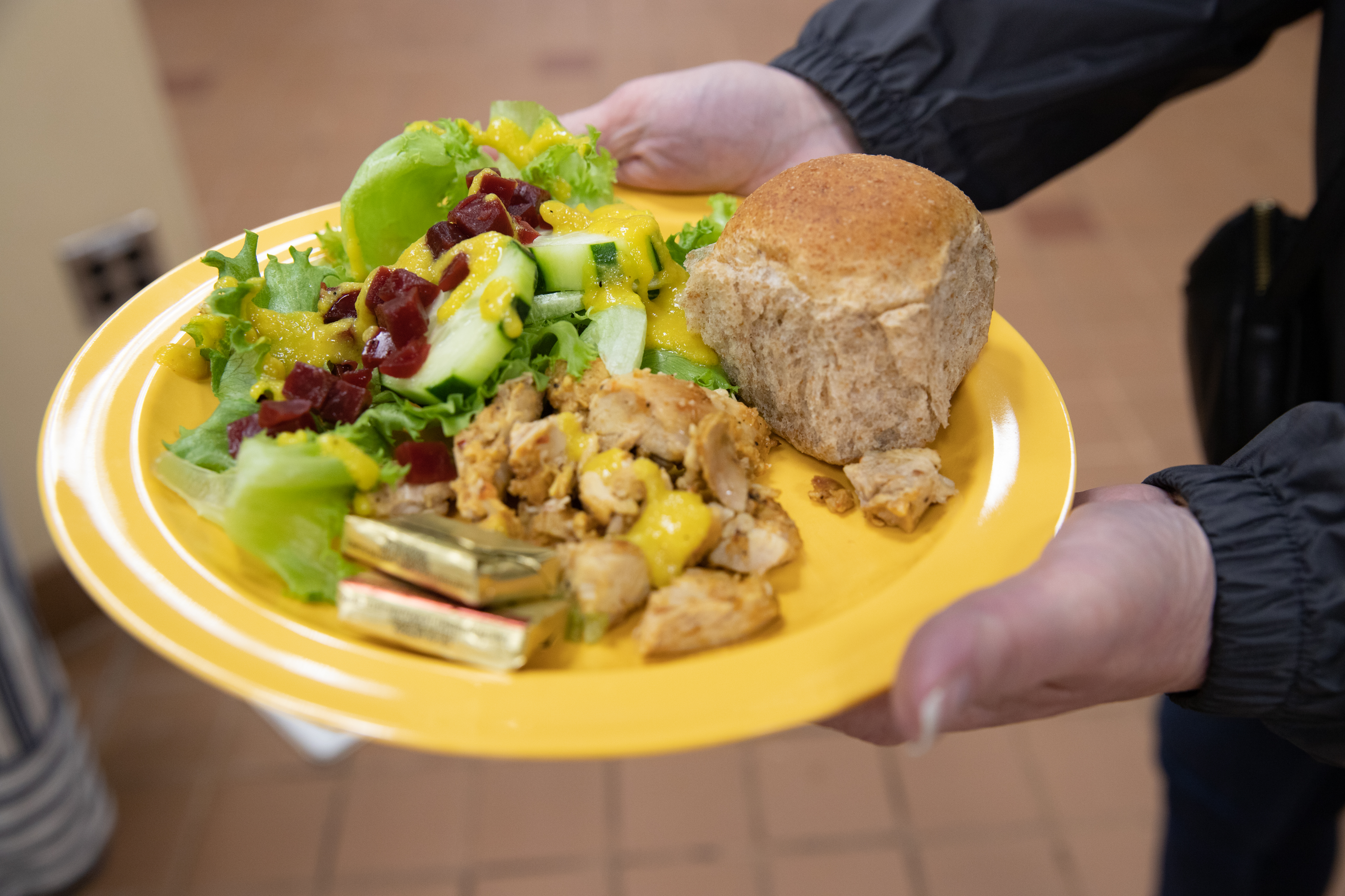 A yellow school cafeteria plate filled with colorful veggies, chicken, and a local roll