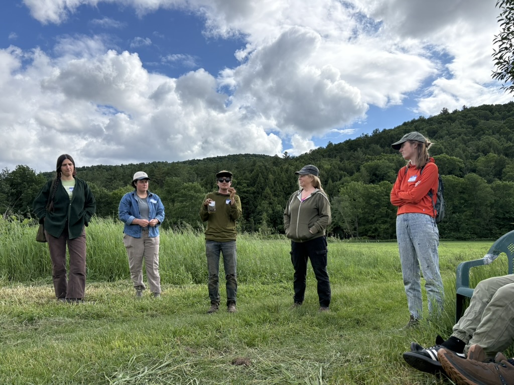 Stoni Tomson of New Tradition Farm and Sarah Jane Williamson of Jubilee Farm stand together in a field speaking to Land Together Learning Network participants about their experience sharing farm land in Huntington