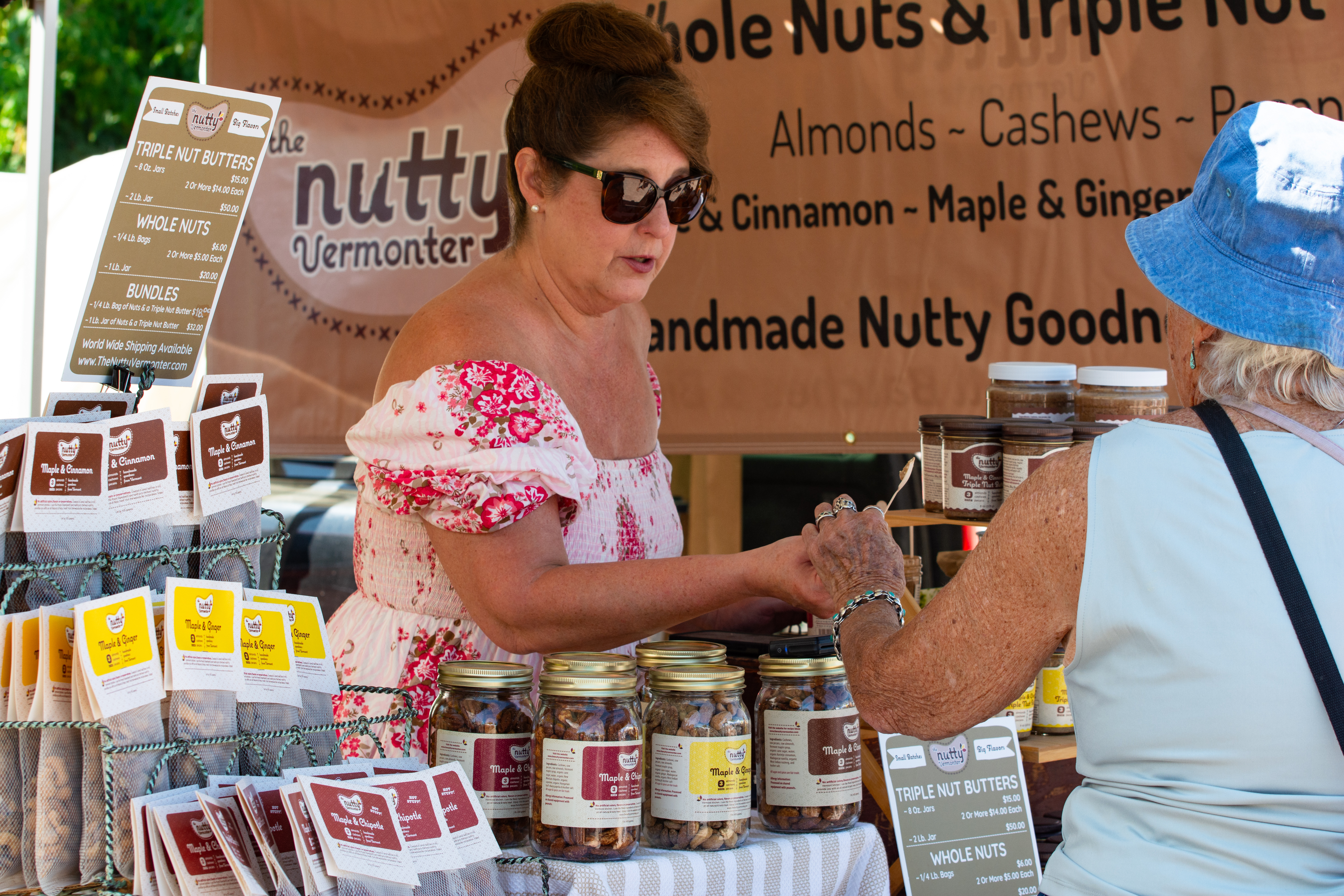 A retailer at a Vermont farmers market accepts payment from a customer across a well-stocked table of local nut butter products
