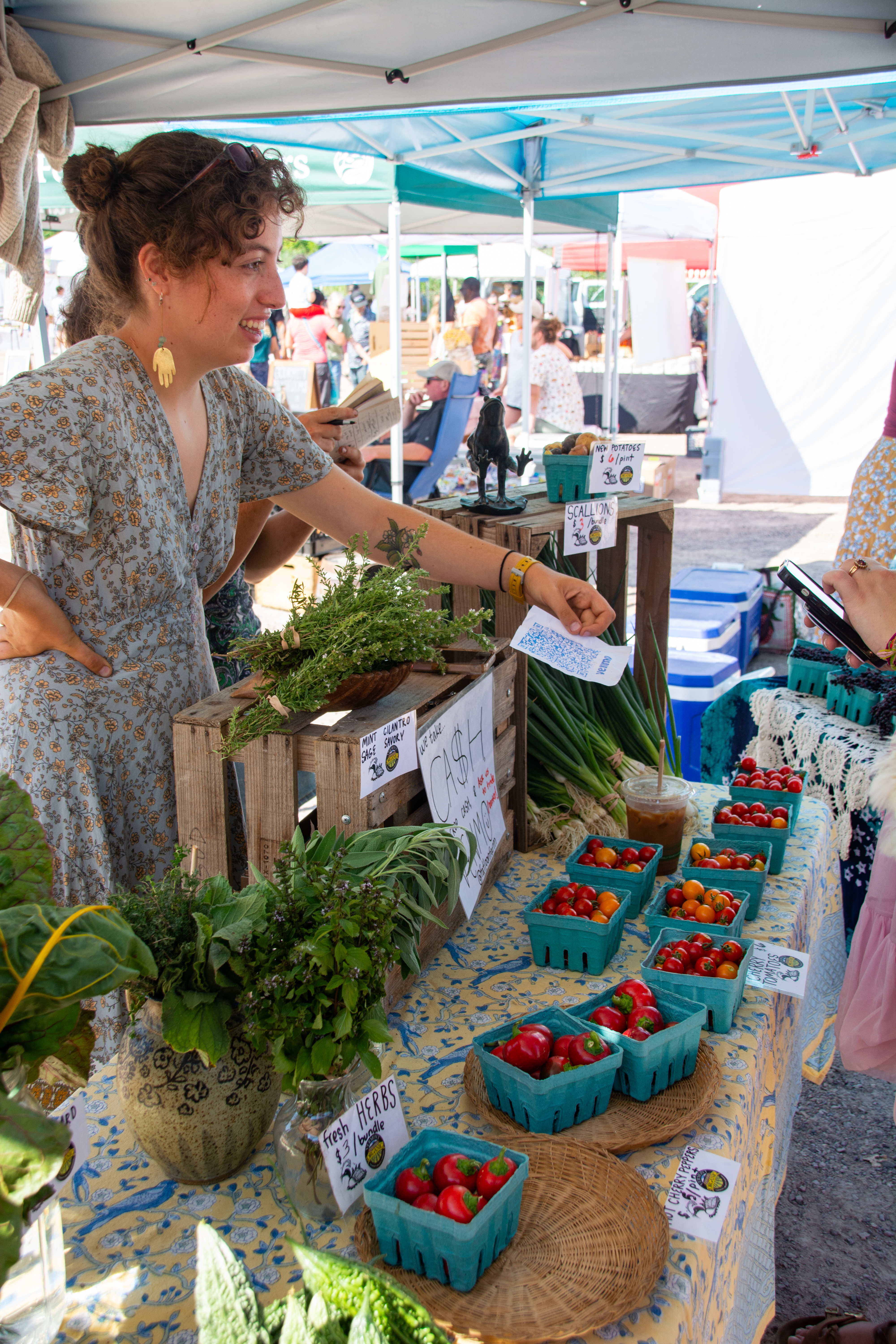 A vendor at a Vermont farmers market holds up a QR code for a customer to scan at her farmers market booth.