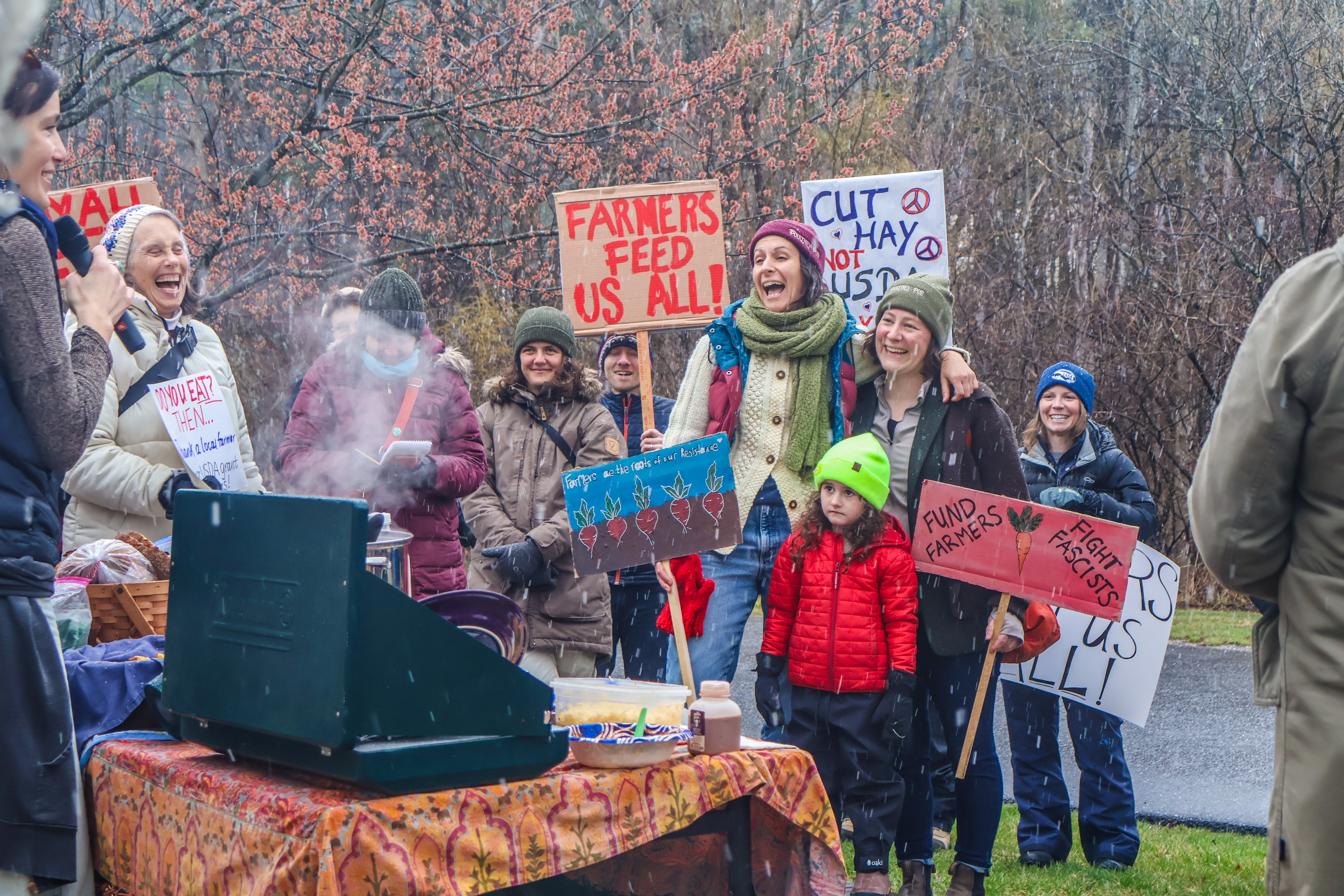 Farmers, farmworkers, and NOFA-VT Members at the Farmer Day of Action at the Middlebury USDA Offices stand holding signs reading "Farmers Feed Us All" and "Cut Hay Not USDA"