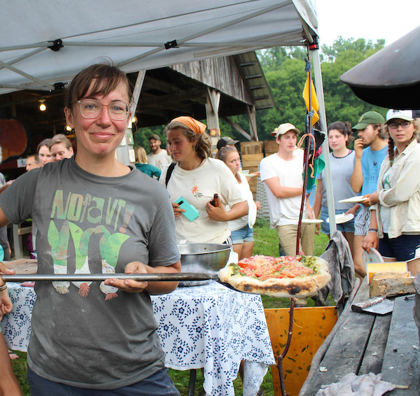 A person serves pizza at an outdoor pizza oven