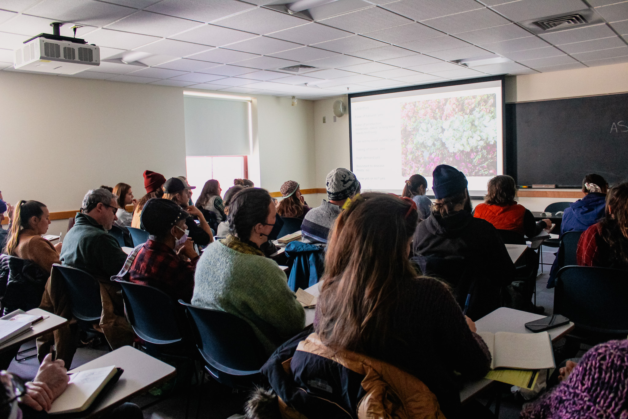 A classroom full of people look at a presentation displaying a farm field.