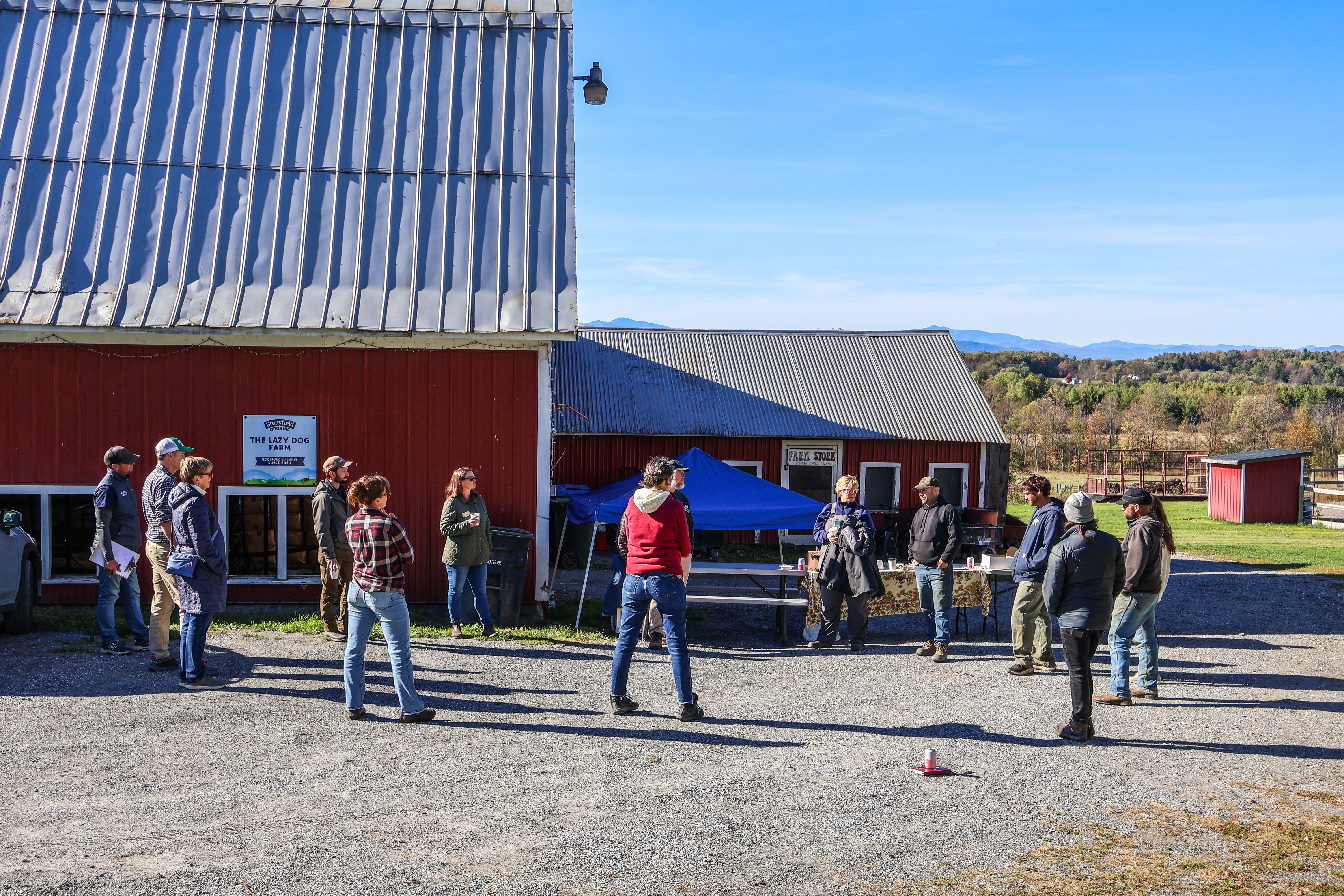 Farmers, legislators, ag support specialists, and members of the NOFA-VT Policy & Advocacy team stand circled up in front of Jesse Wilbur's barn at Lazy Dog Farm in Orwell