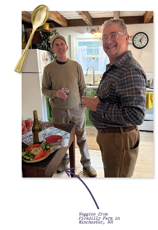 Two people smile in a kitchen, standing over a plate of cucumbers and carrots.