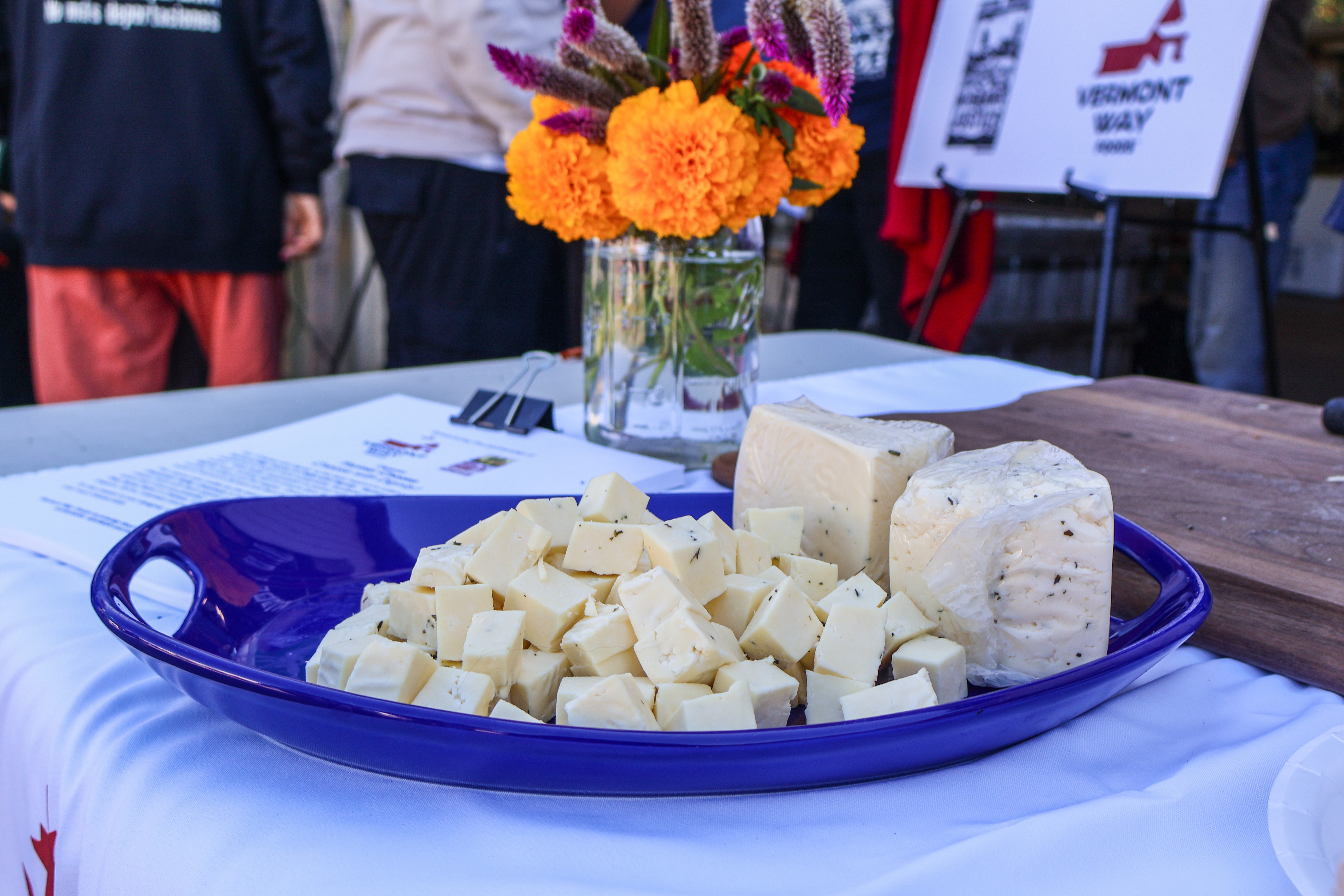 the first certified organic, Milk With Dignity-sourced cheese sits on a table with a vase of flowers and a group of migrant farmworkers signing the Milk With Dignity agreement with Vermont Way Foods in the background