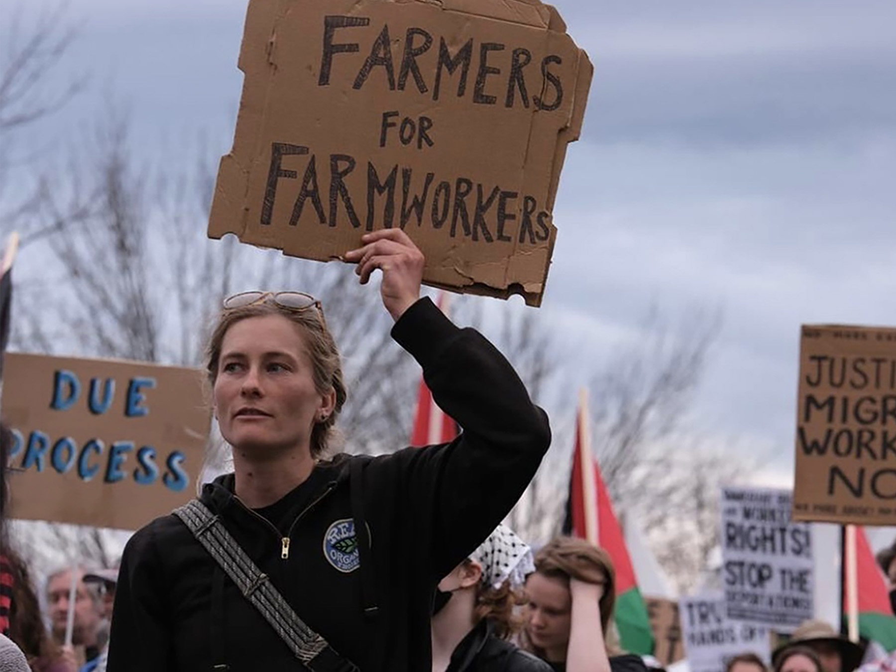 NOFA-VT Farmer-member Mollie of Glinnis Hill Farm marches proudly with a handmade cardboard sign reading "Farmers for Farmworkers" at a Migrant Justice May Day rally in Williston, VT