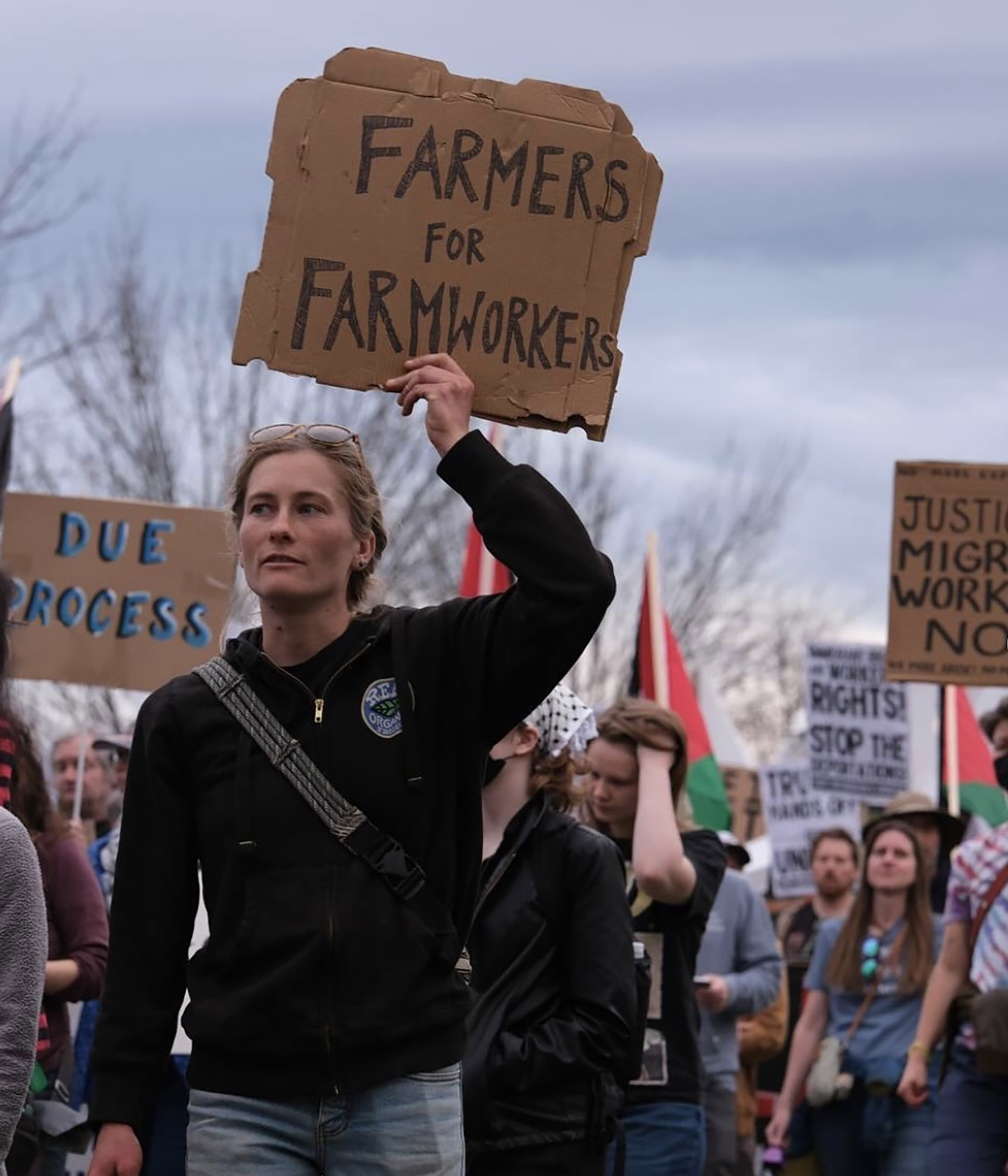 Farmer Mollie of Glinnis Hill Farm marching at a Migrant Justice event with a banner that reads "Farmers for Farmworkers"