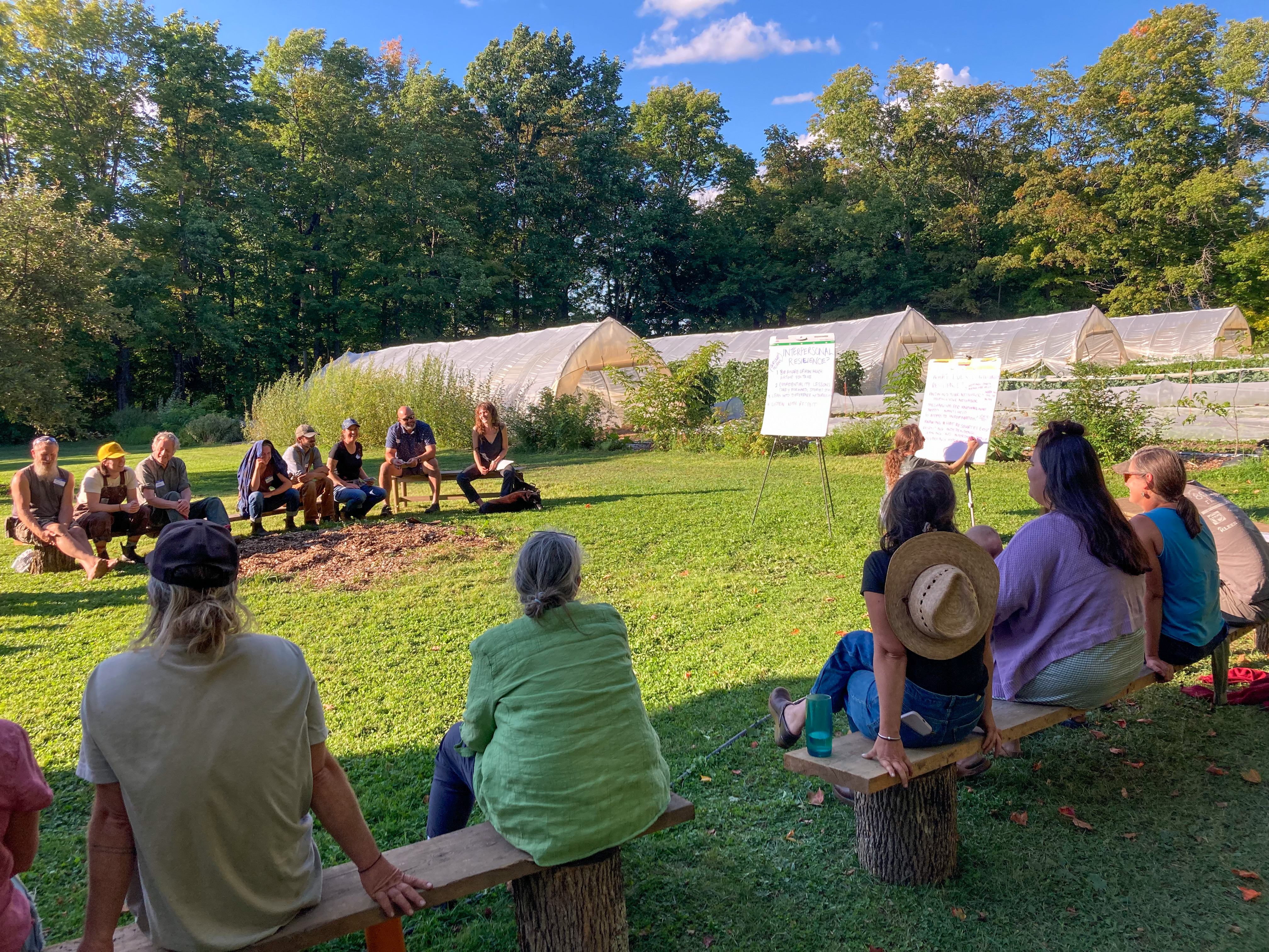 Participants in the NEK Resilience Project gathered in a circle at Breadseed Farm sharing ideas about the collaboration on large flip charts with Breadseed's high tunnels in the background