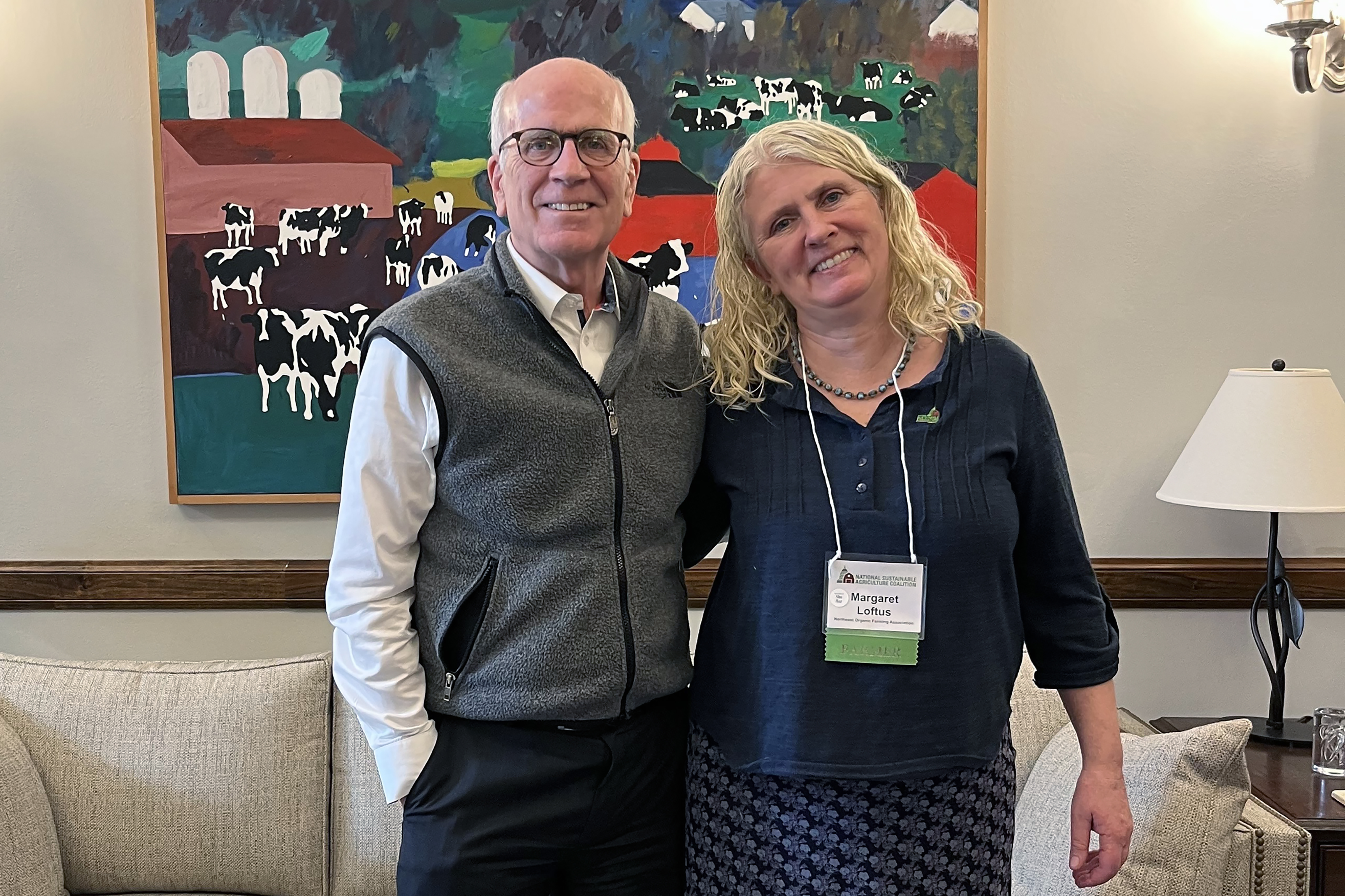 NOFA-VT farmer-member Margaret Loftus of Crossmolina Farm is pictured standing arm-in-arm with Senator Peter Welch in his office in DC. There is a Woody Jackson cow painting on the wall behind them.