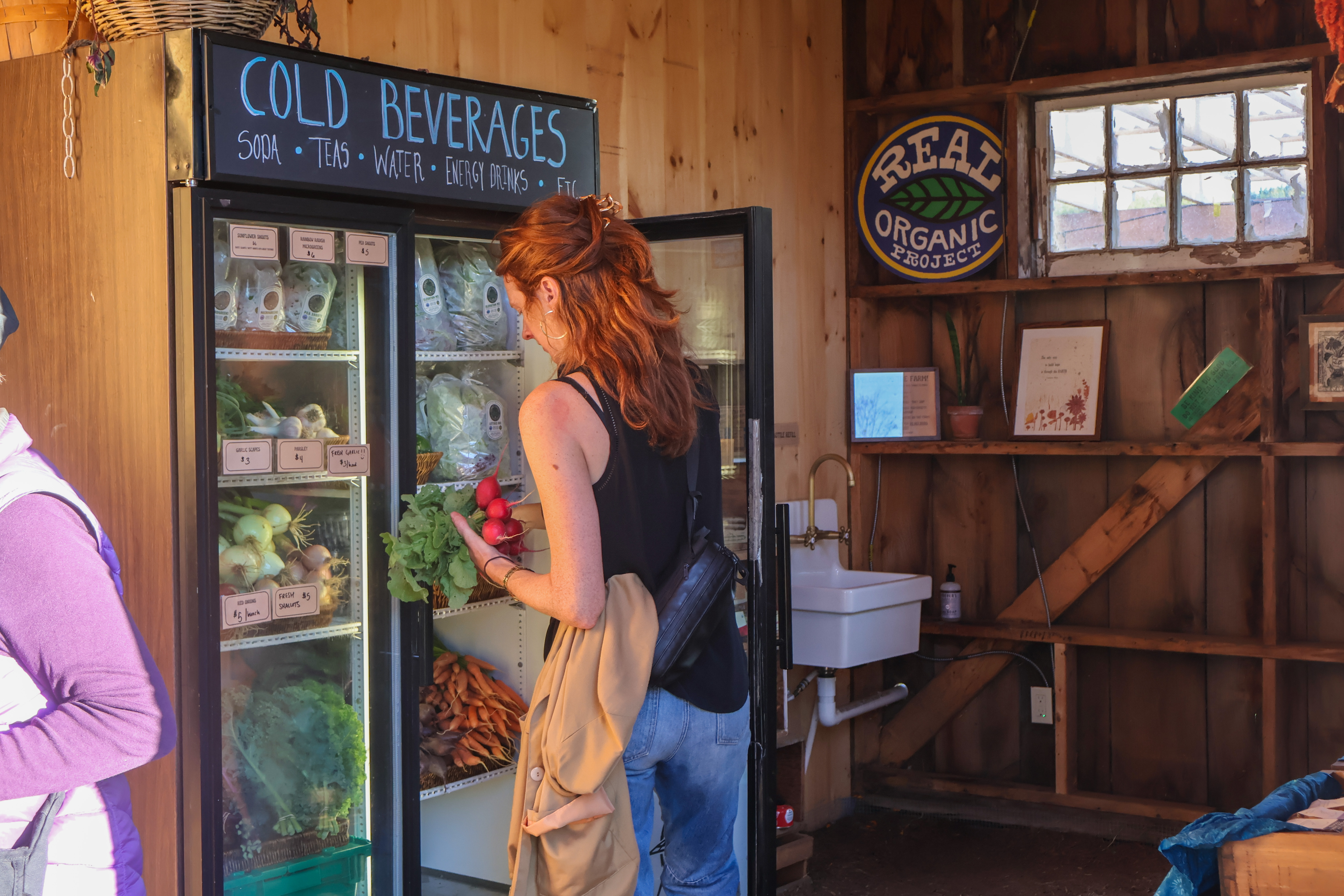 A shopper takes a bundle of radishes from the farmstand refrigerator at Stone's Throw Farmstead