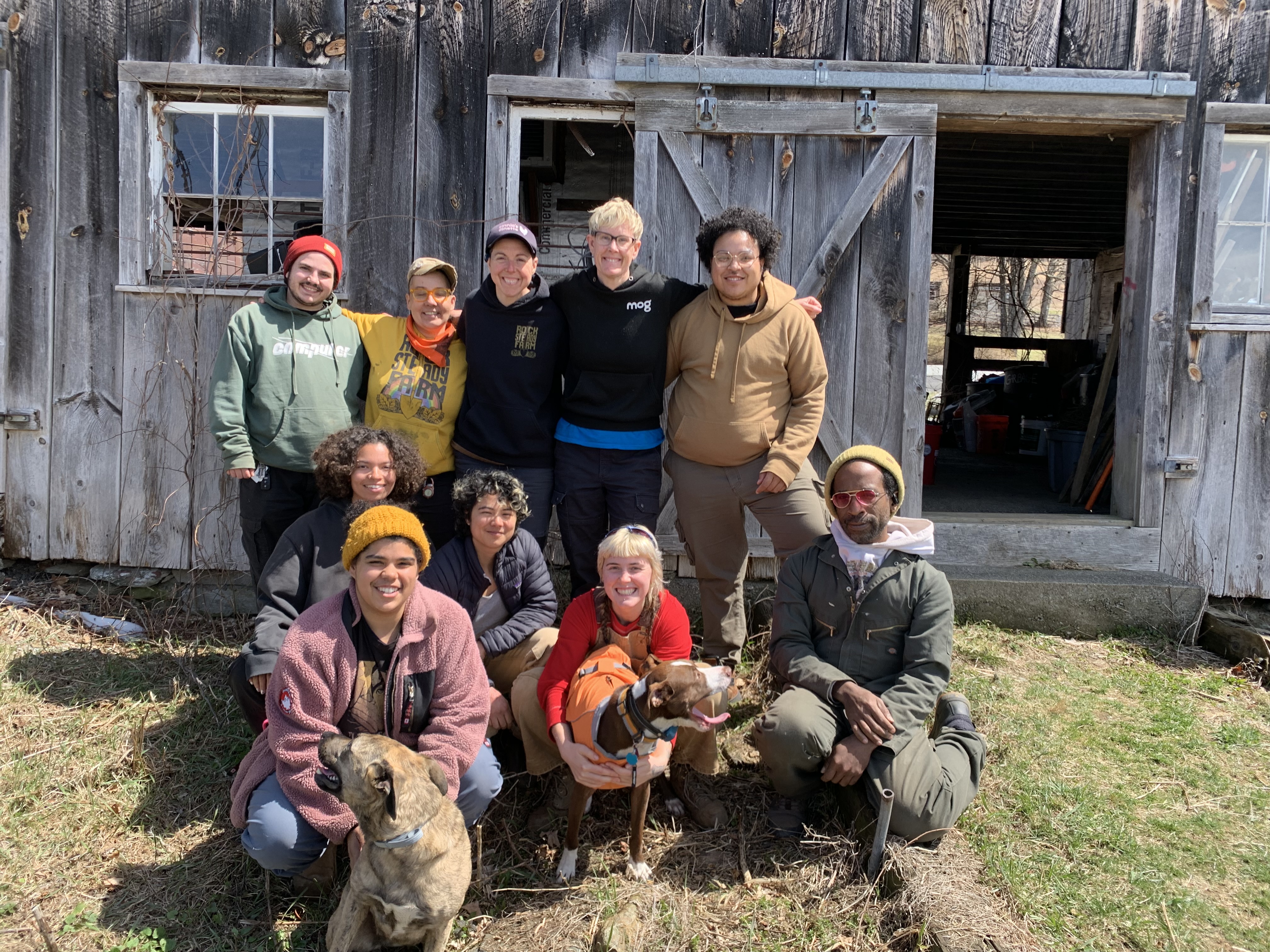A smiling group of farmers from Rock Steady Farm stand arm-in-arm in front of their barn
