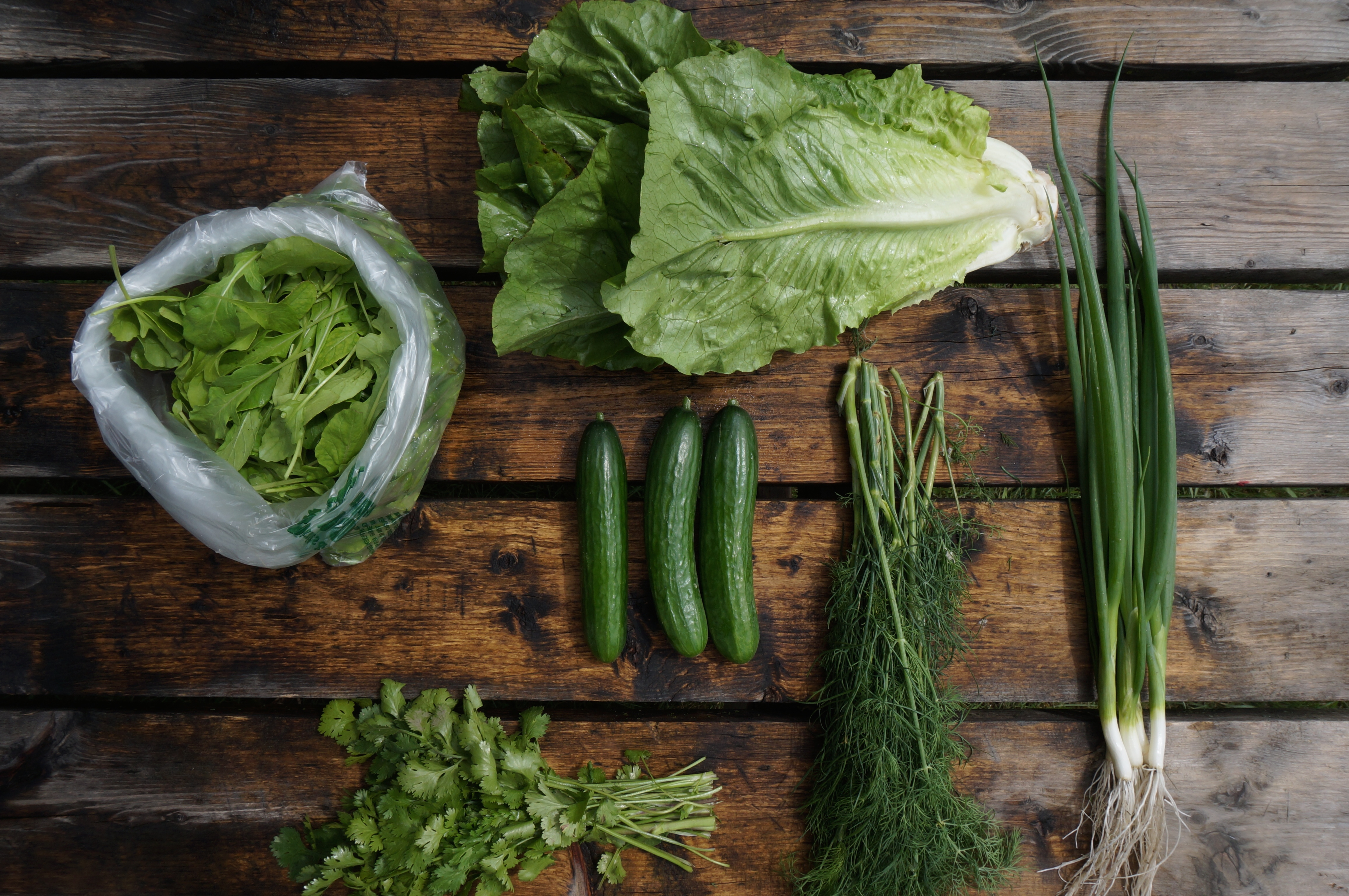 An array of green veggies from a CSA spread out on a wooden table