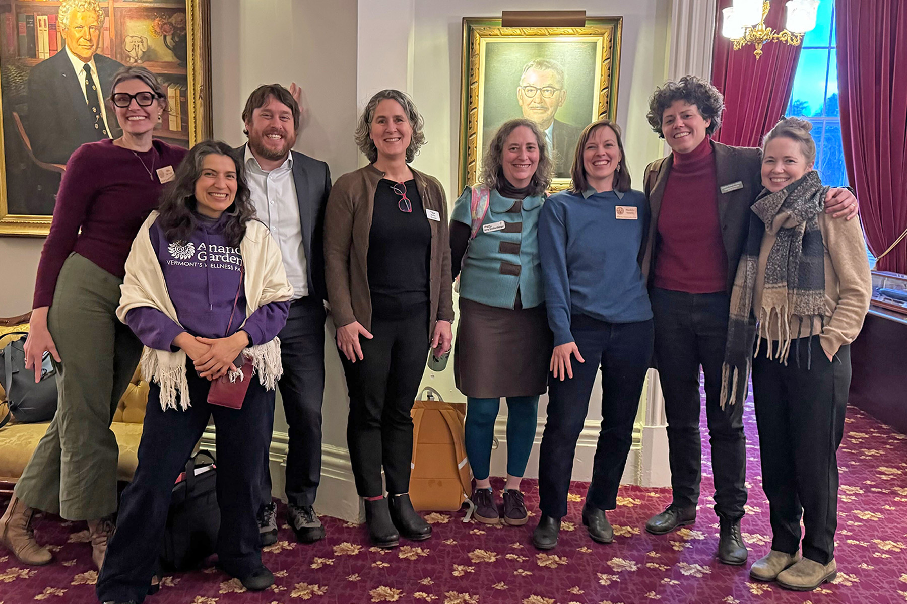 NOFA-VT Grassroots Organizer Jess Hays Lucas and NOFA-VT Policy & Organizing Director, Maddie Kempner, stand smiling in a group shot at the State House with other coalition allies, including NOFA-VT farmer-member Melisa Oliva of Ananda Gardens, Jake Claro of Vermont Farm to Plate, Vermont Food Security Coalition Director Becka Warren, Action Circles director Amy Schollenberger, Rural Vermont Legislative Director Caroline Gordon, and Vermont Farm Fund manager Kristin Blodgett