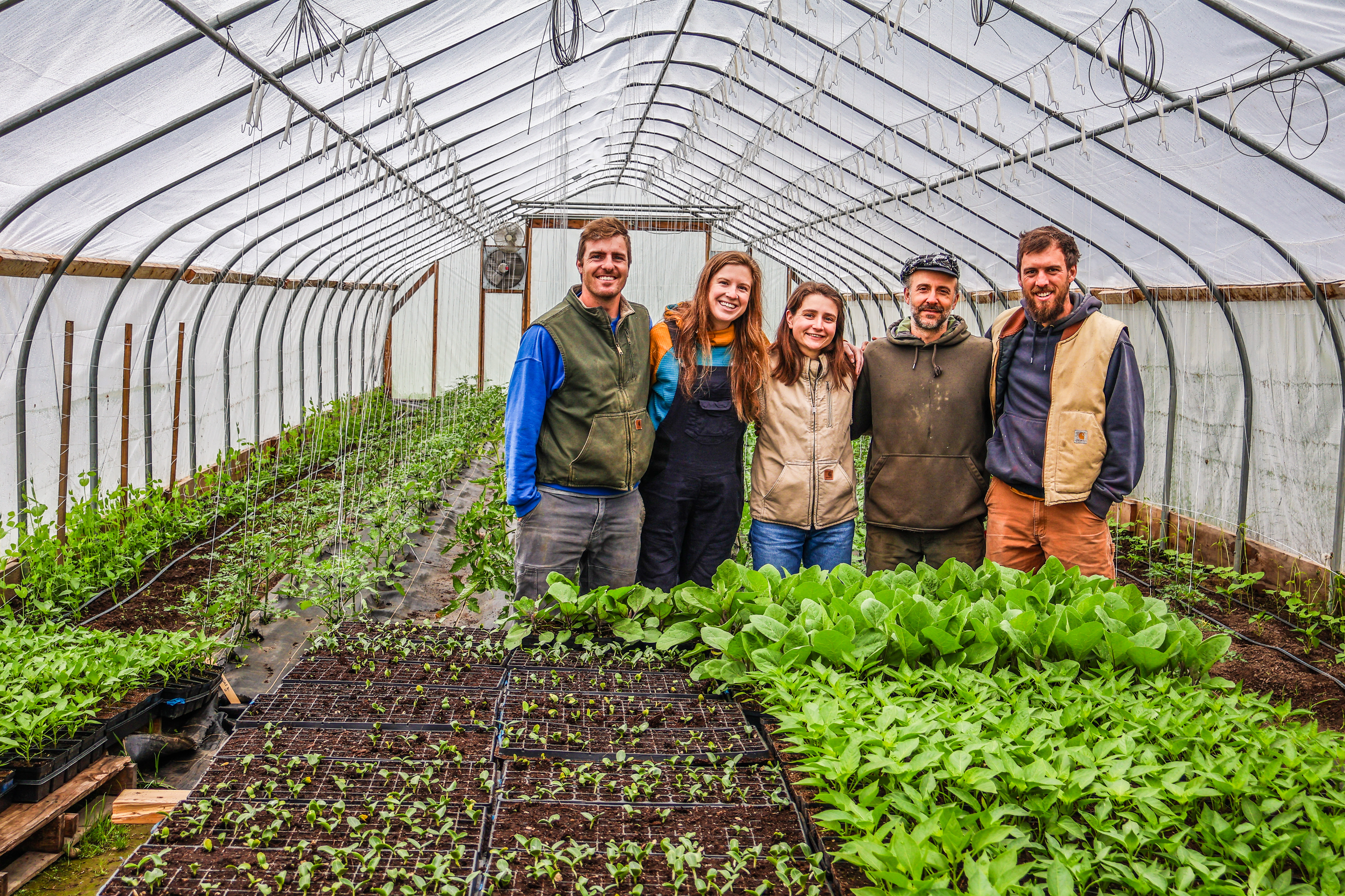 Jake, Cory, Tucker, Spencer, and Jacqueline of the Farm Upstream stand in their high tunnel full of spring plantings