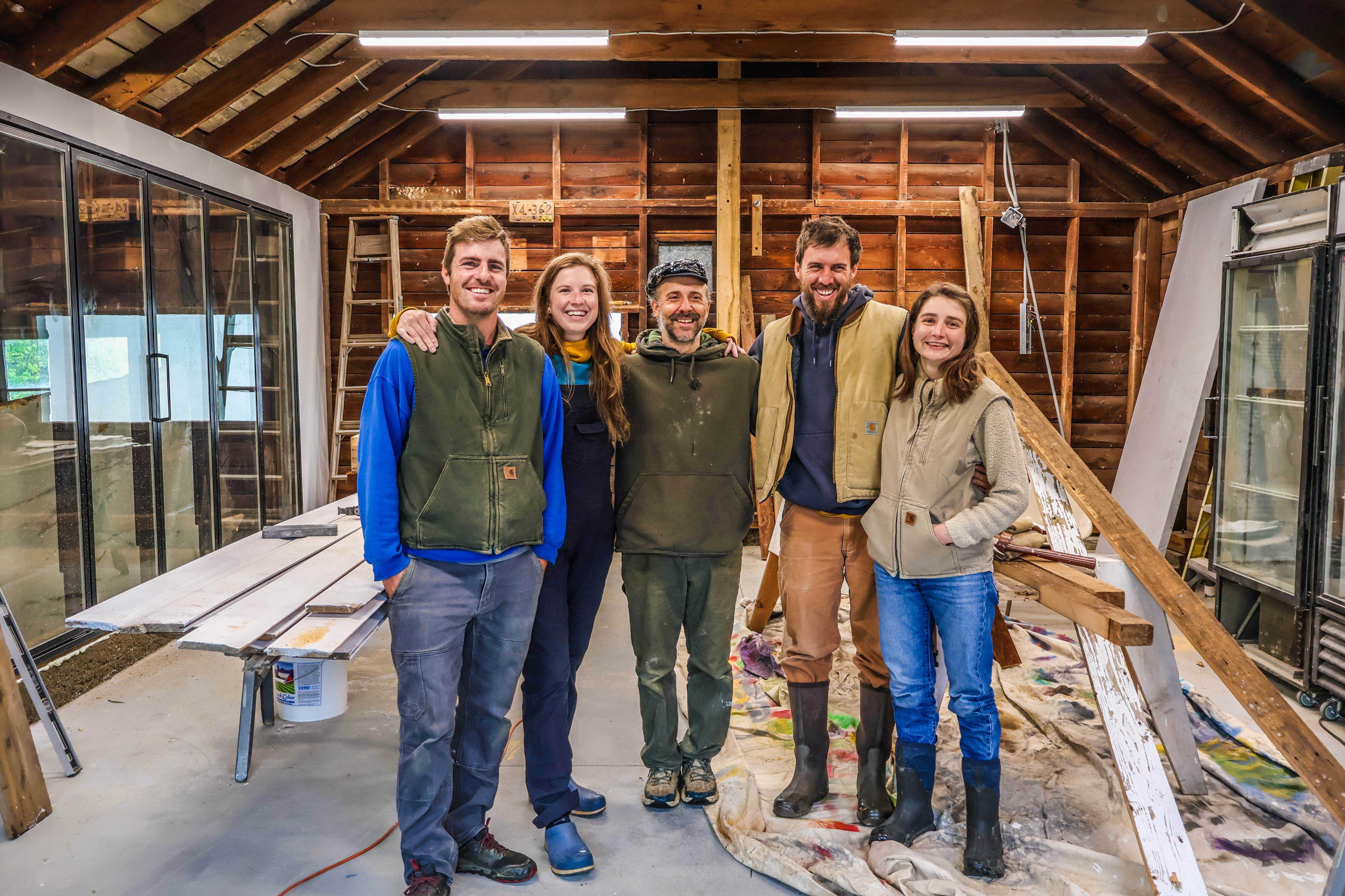 Cory Froning, Jake Kornfeld , Tucker Andrews, Spencer Hardy, and Jacqueline Huettenmoser of The Farm Upstream stand smiling together in their farm stand as it is still under construction