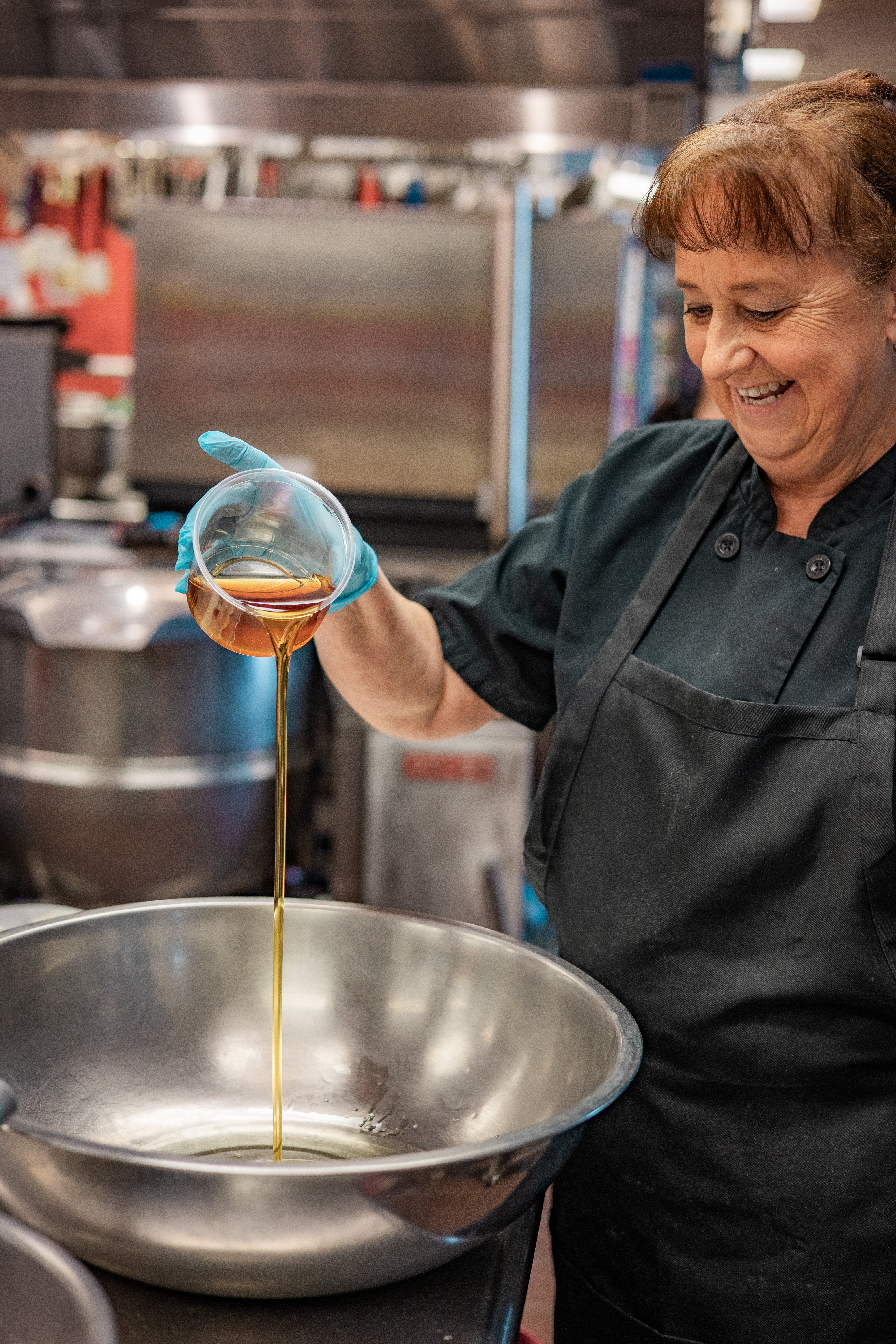 A food service professional smiles while pouring local maple syrup into a large stainless steel bowl