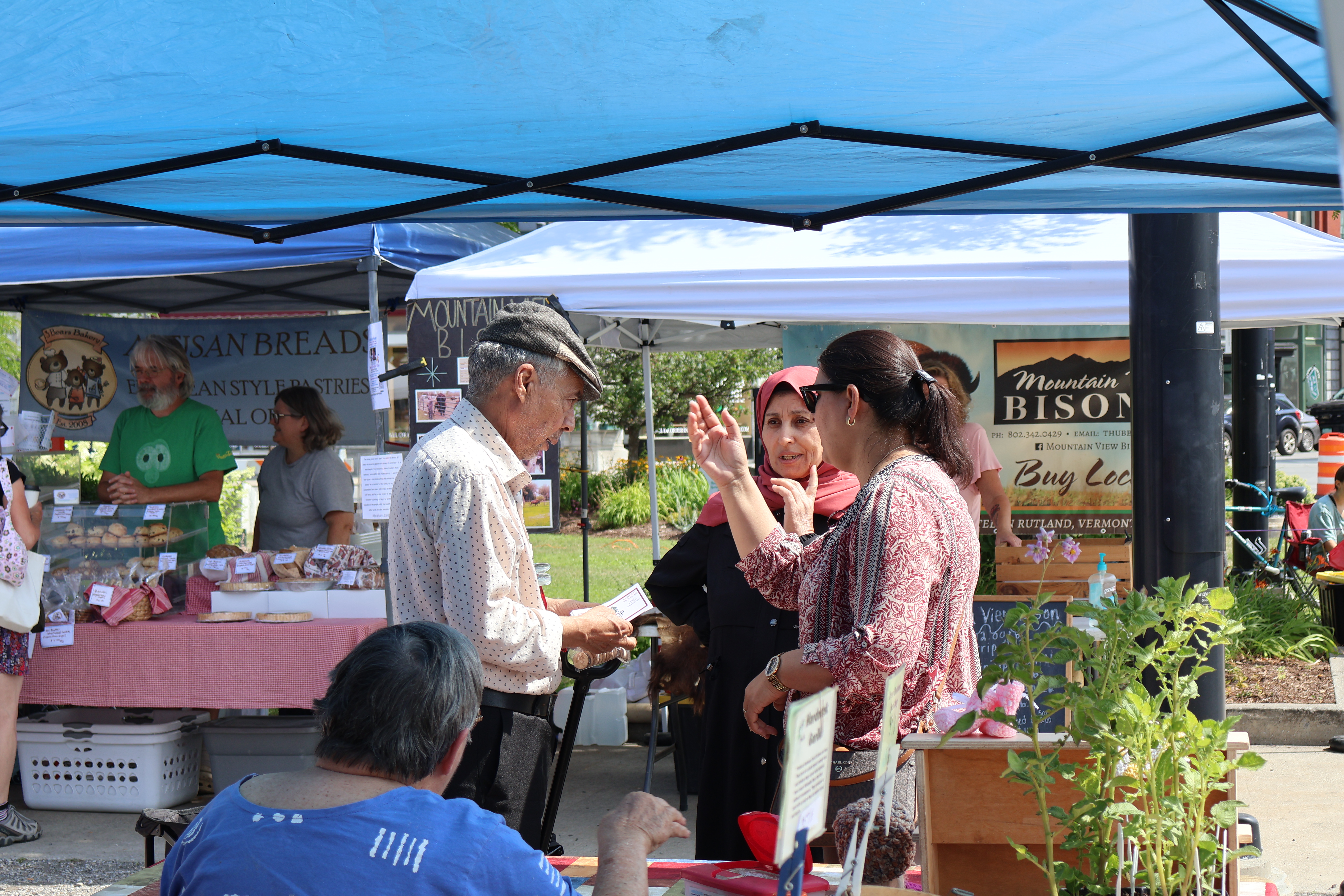 shoppers at the Vermont Farmers Market in Rutland chat together in front of a row of market booths.