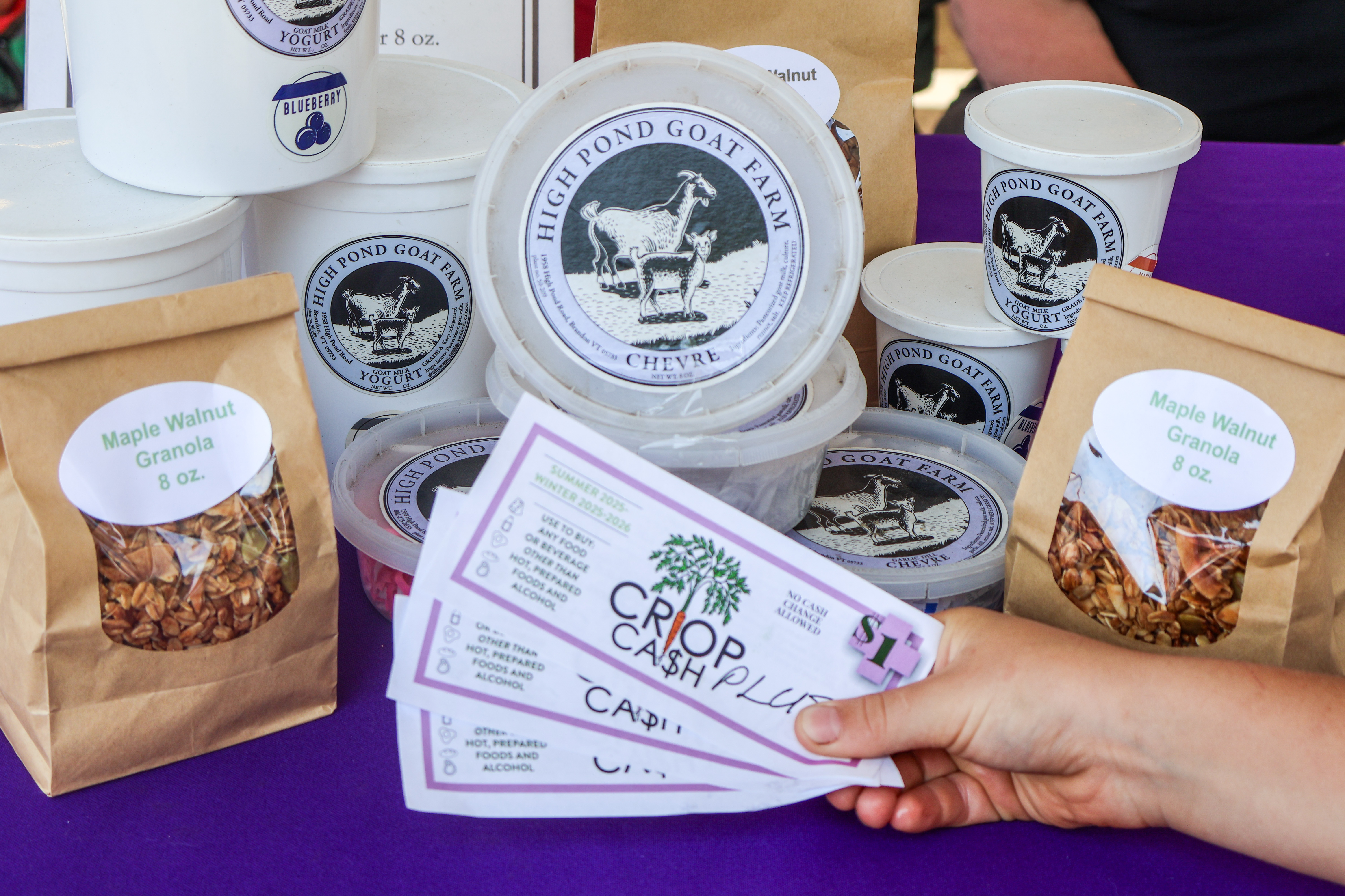 Crop Cash PLUS coupons fanned out in front of an array of eligible products including granola, yogurt, and cheese from High Pond Goat Farm