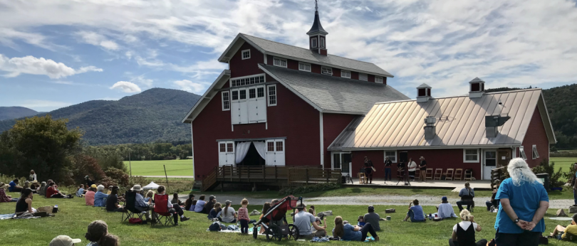 People sit on a lawn near a barn.