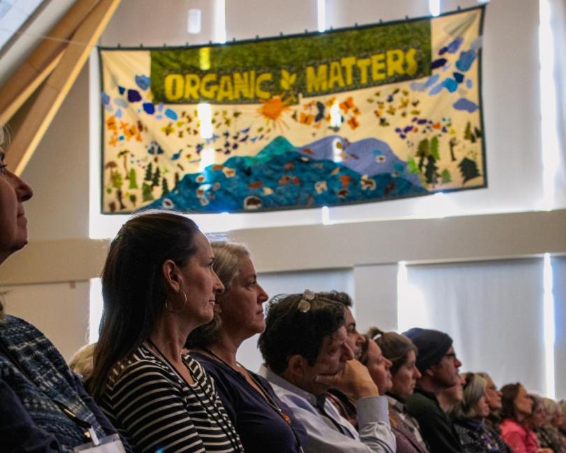 People in an audience below a quilt that reads "organic matters"