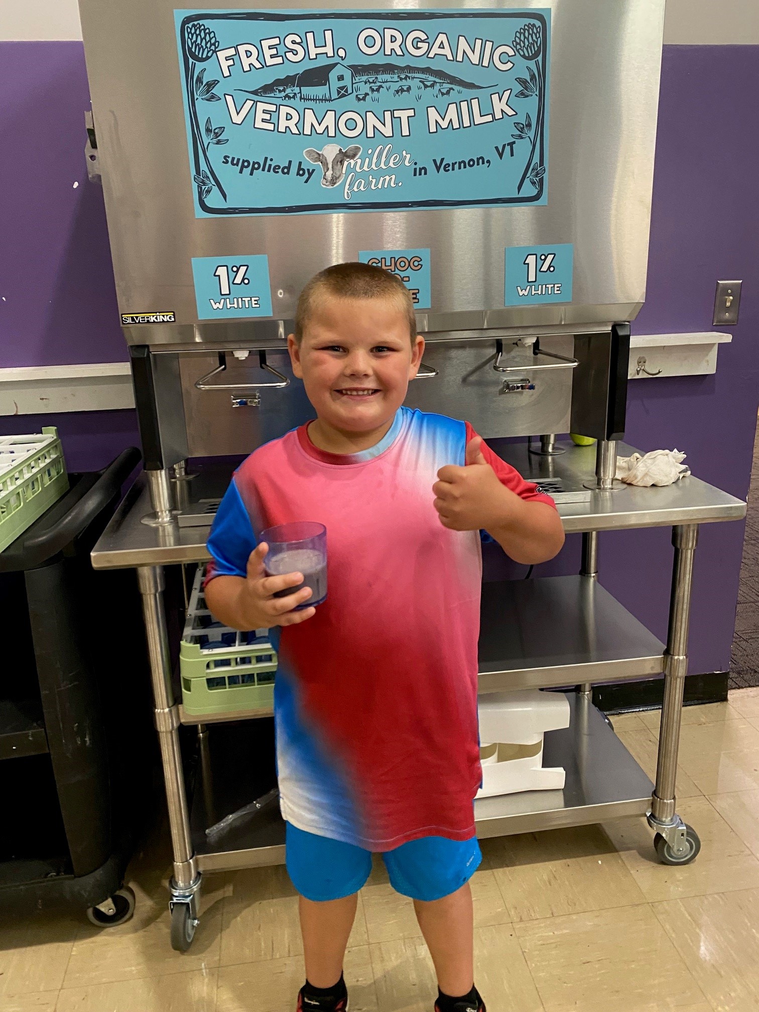 A kid gives a thumbs up a milk dispenser in a cafeteria