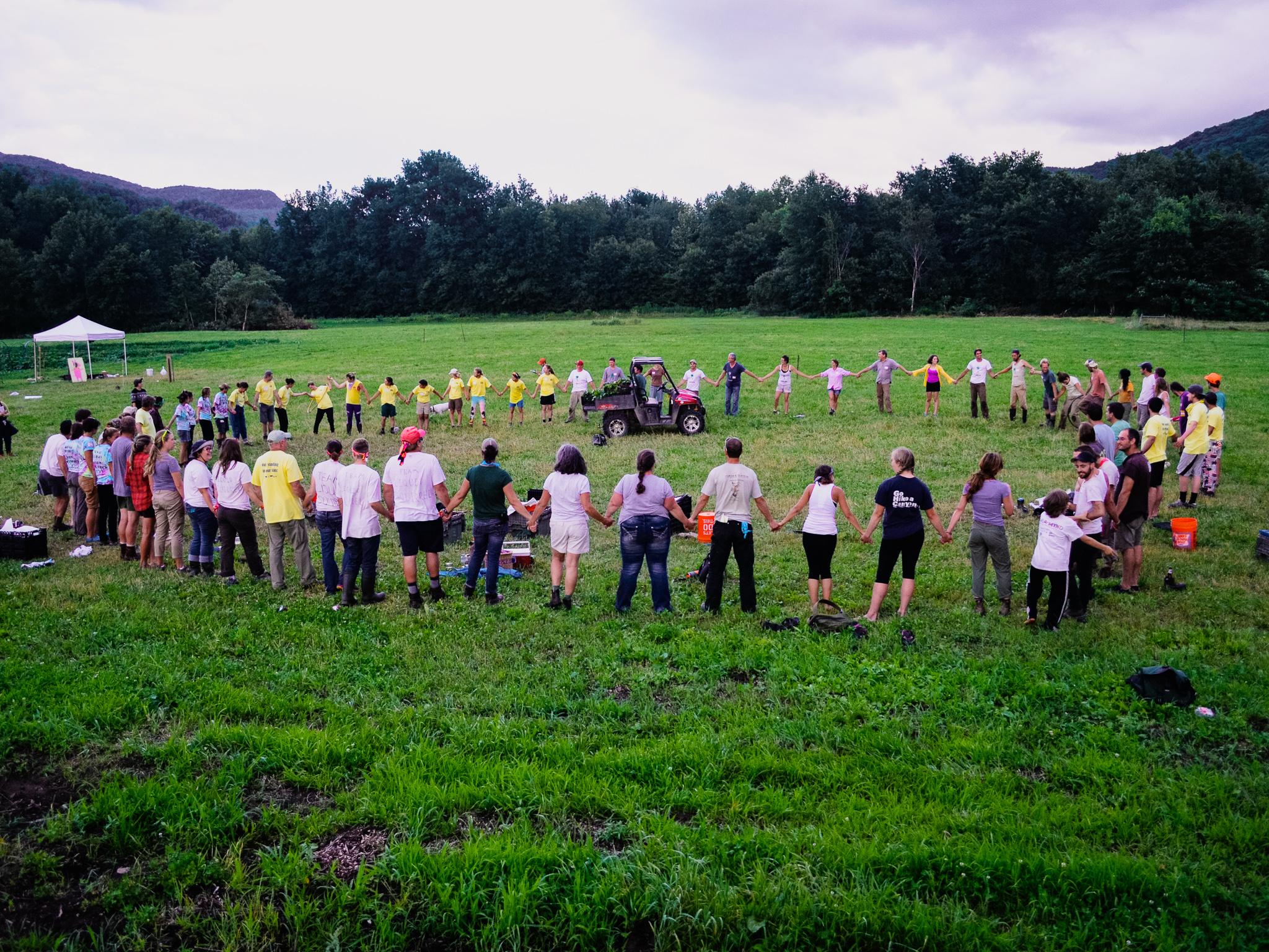A large group of people stands on a field holding hands in a circle.