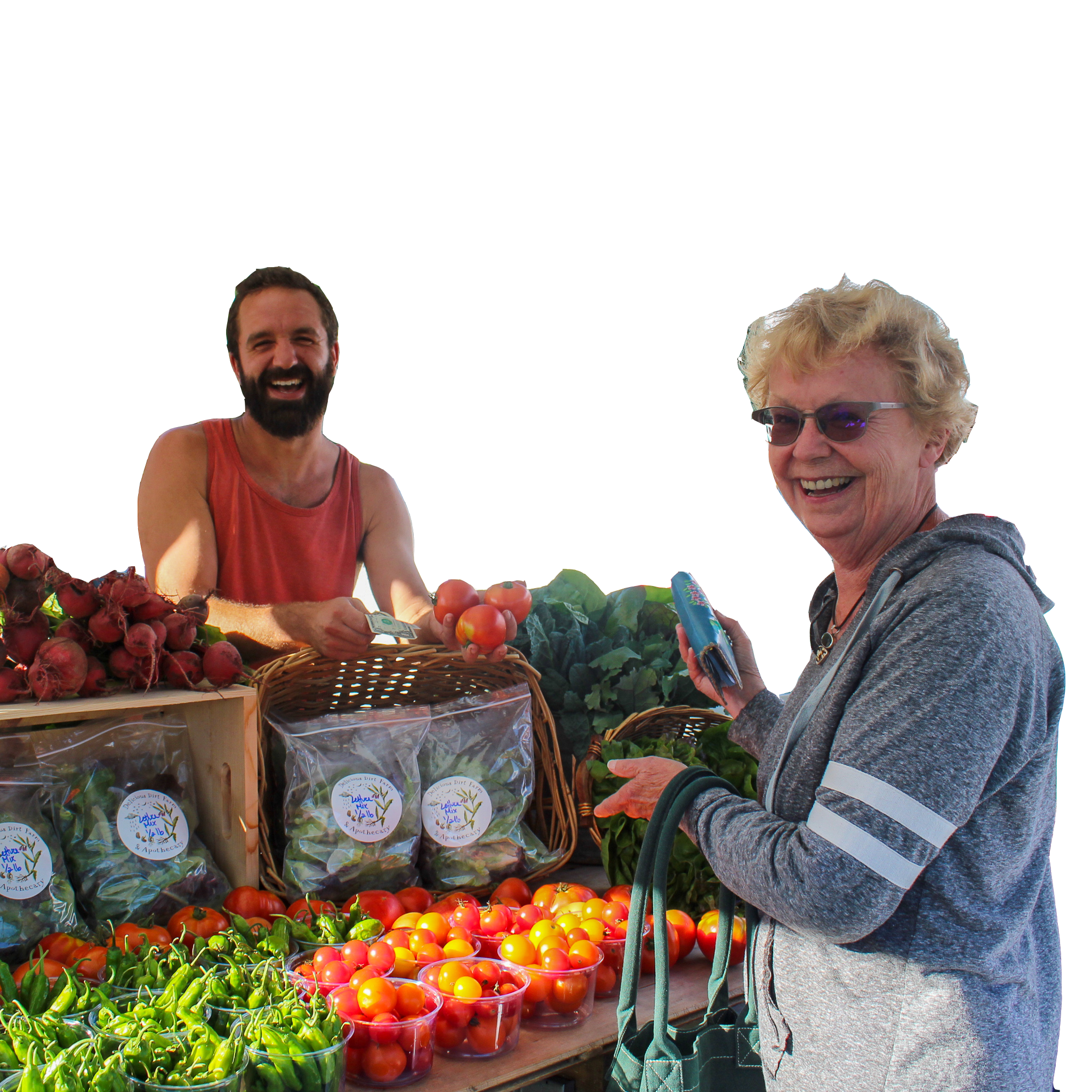 A farmer stands behind a table of produce, smiling at the camera. Another person is standing in front of the table, also smiling and holding a wallet.