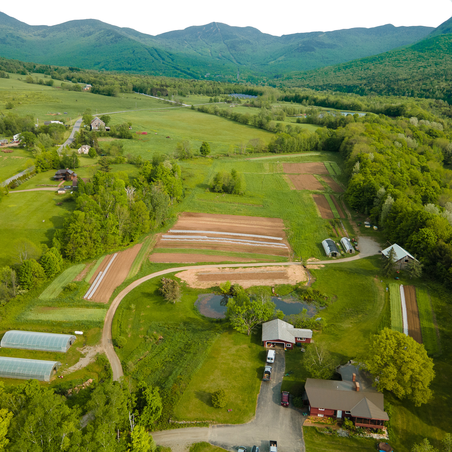 A farm field is seen from above, with rolling mountains in the background.