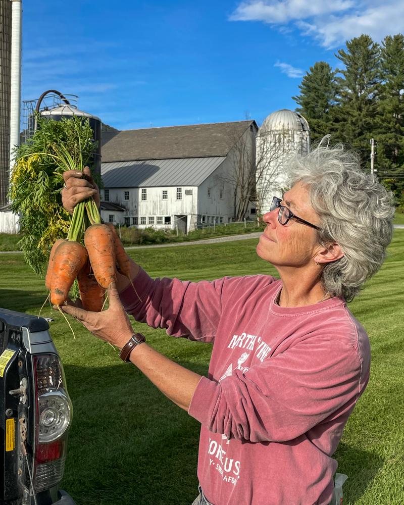 Maria, a farmer, holds up a clump of carrots, admiring them.