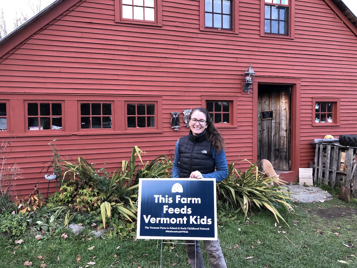 Misse stands outside with a sign that reads "this farm feeds VT kids"