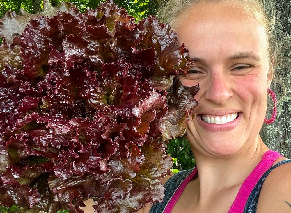 Emma smiles at the camera, holding a bundle of lettuce