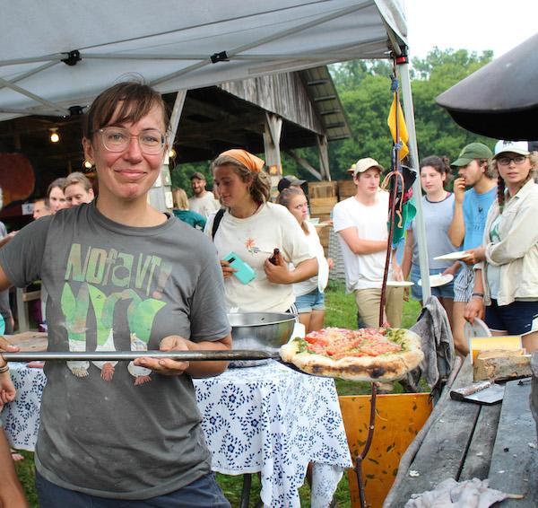 A person serves pizza at an outdoor oven
