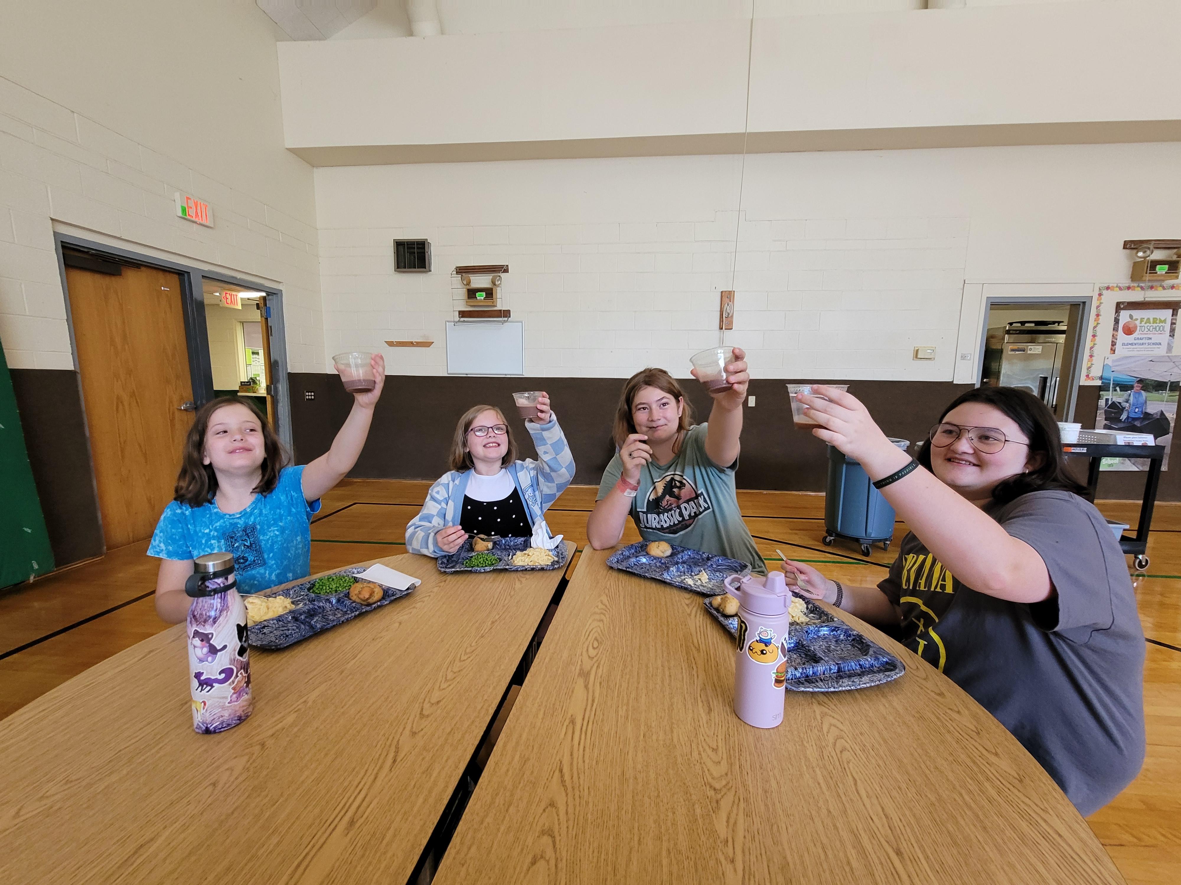 Kids raise up cups of milk in a "cheers" motion around a lunch table