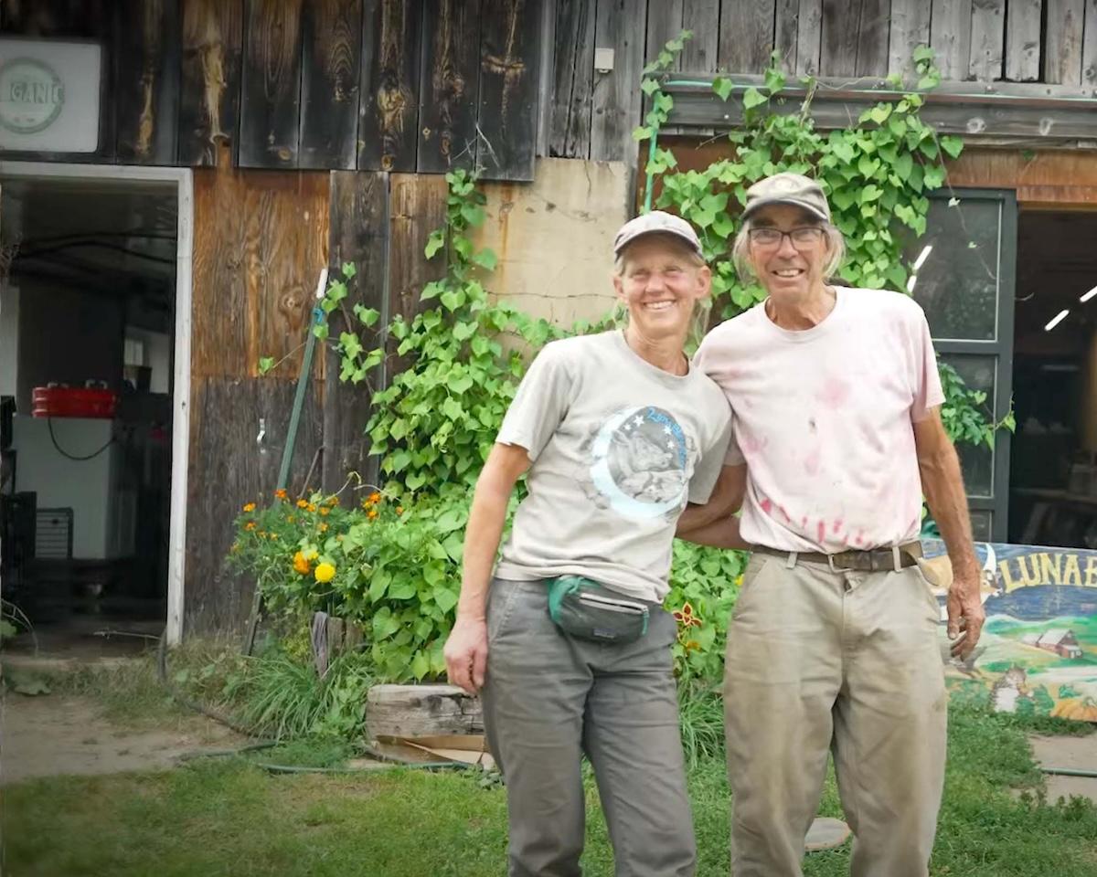 Two farmers stand outside their barn, smiling