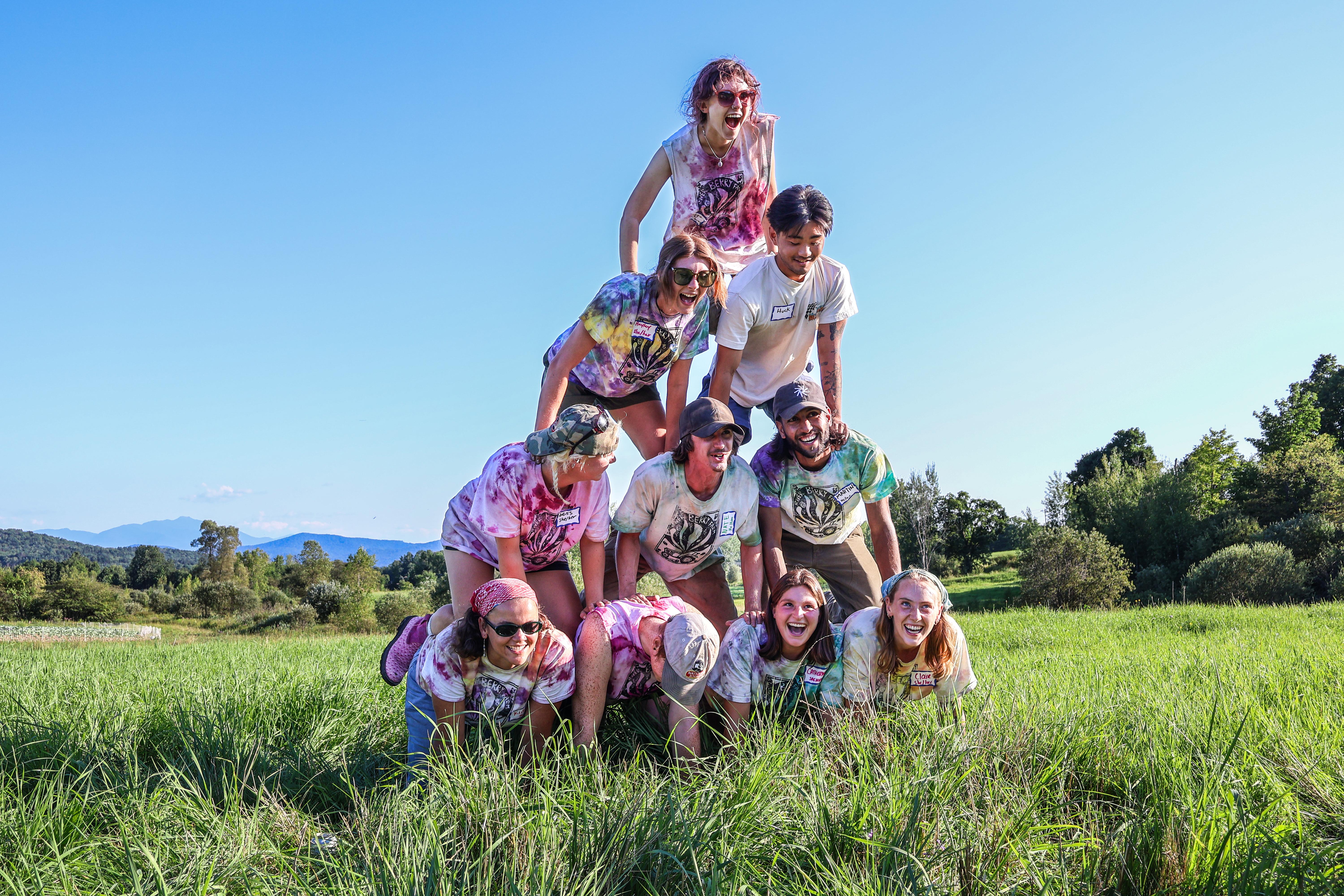 Farmers and farmworkers wearing huge grins and matching tie-dye tees as they make a human pyramid at the 2024 Farmer Olympics 