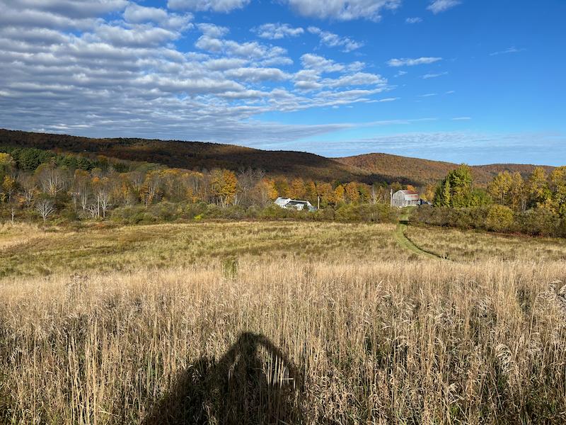 A view of a Vermont farm field looking down a hill toward a farmhouse and barn