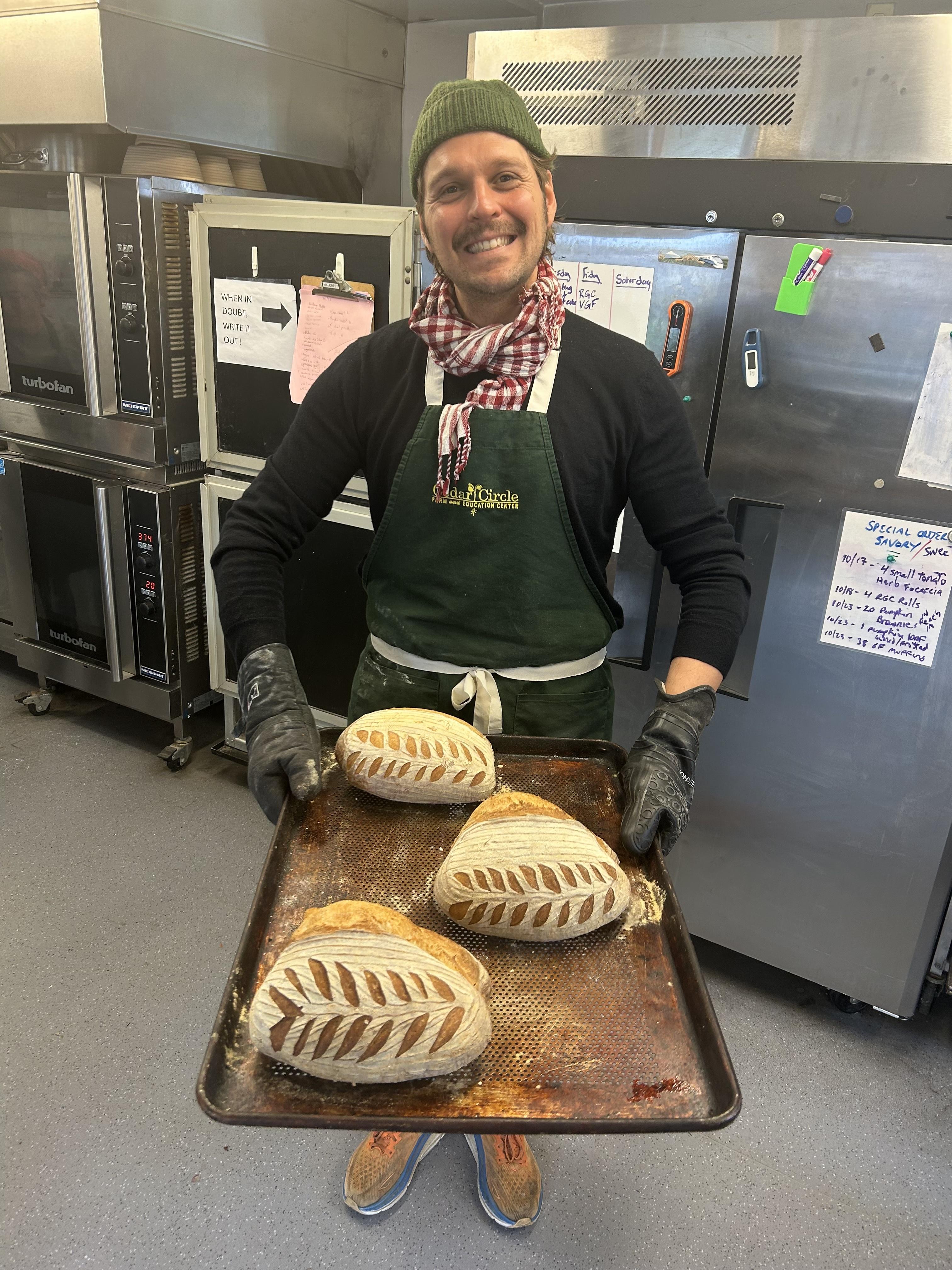 Baker holding tray of sourdough loaves
