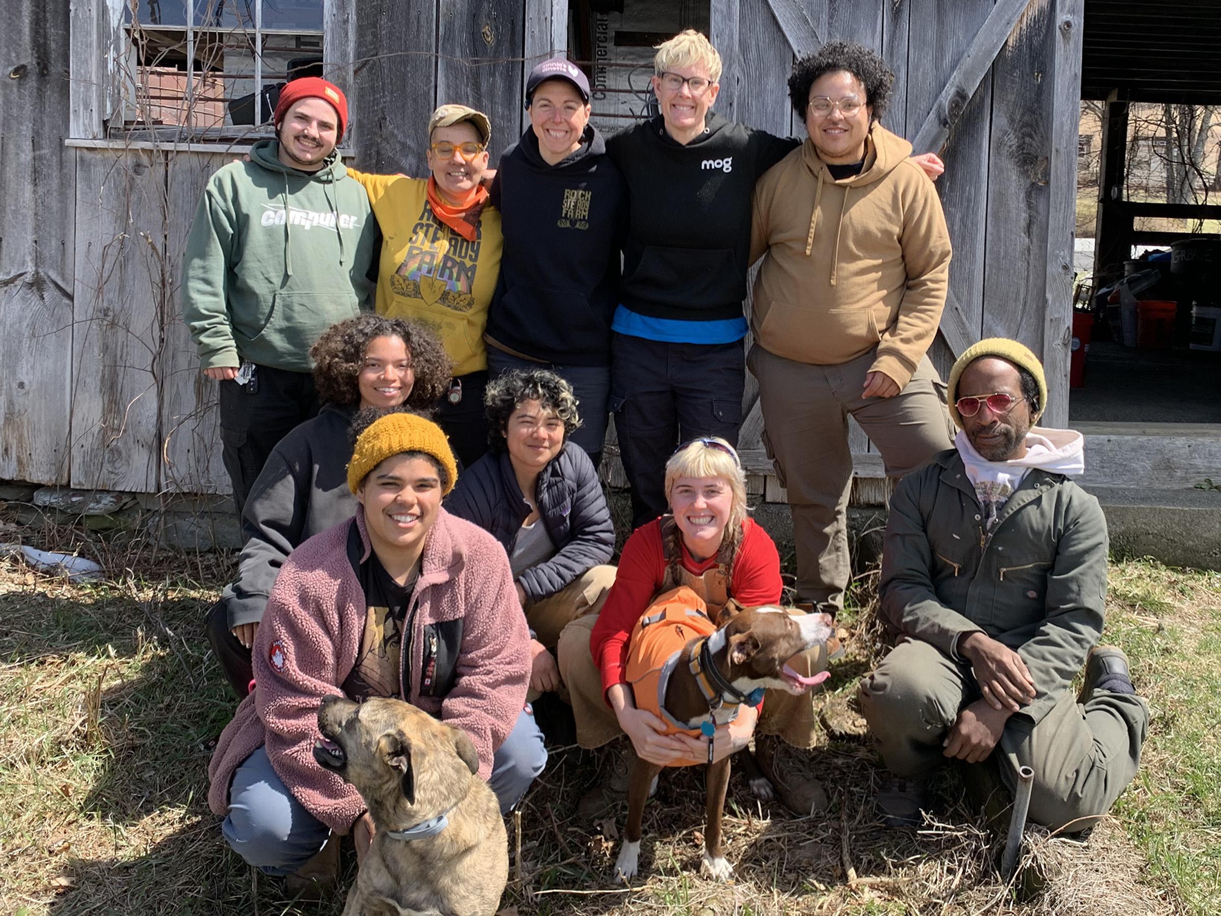 A group photo of the farmers that make up Rock Steady Farm posting with smiles and a few farm dogs in front of their barn