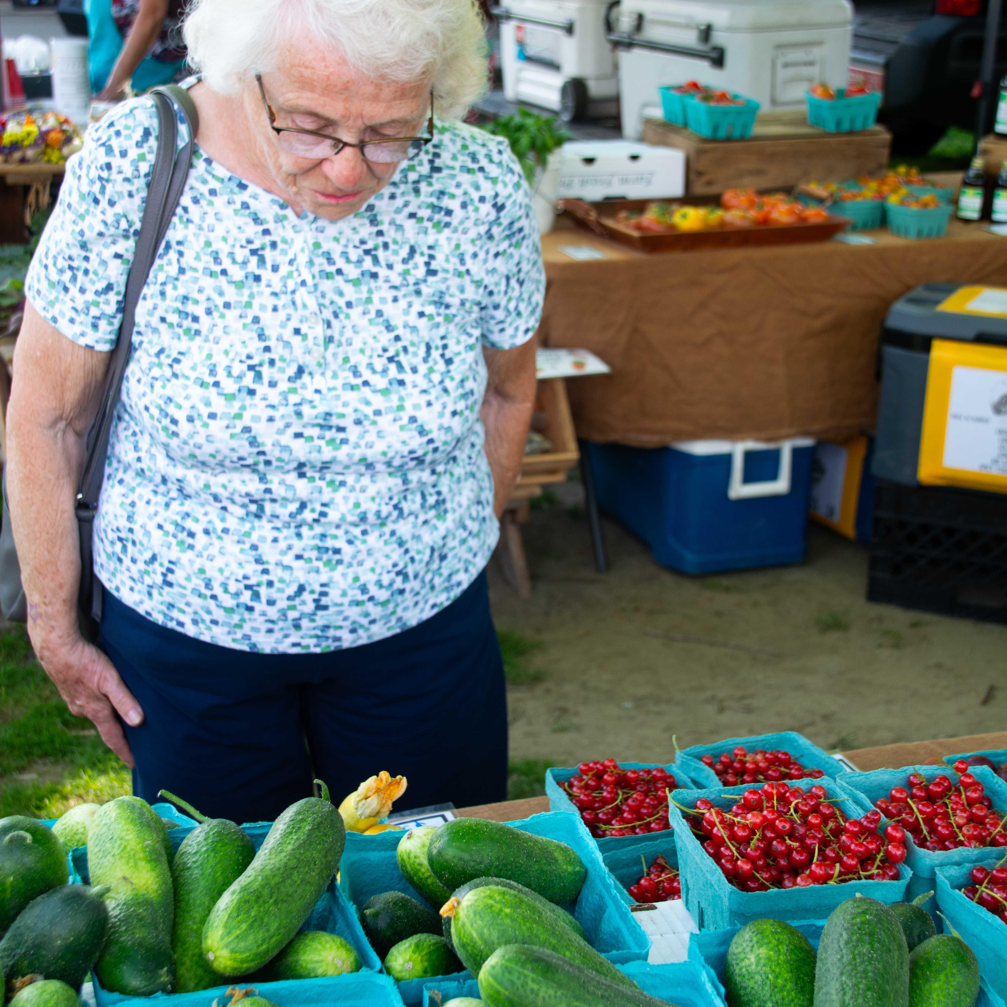 An older Vermonter stands admiring a table full of fresh veggies