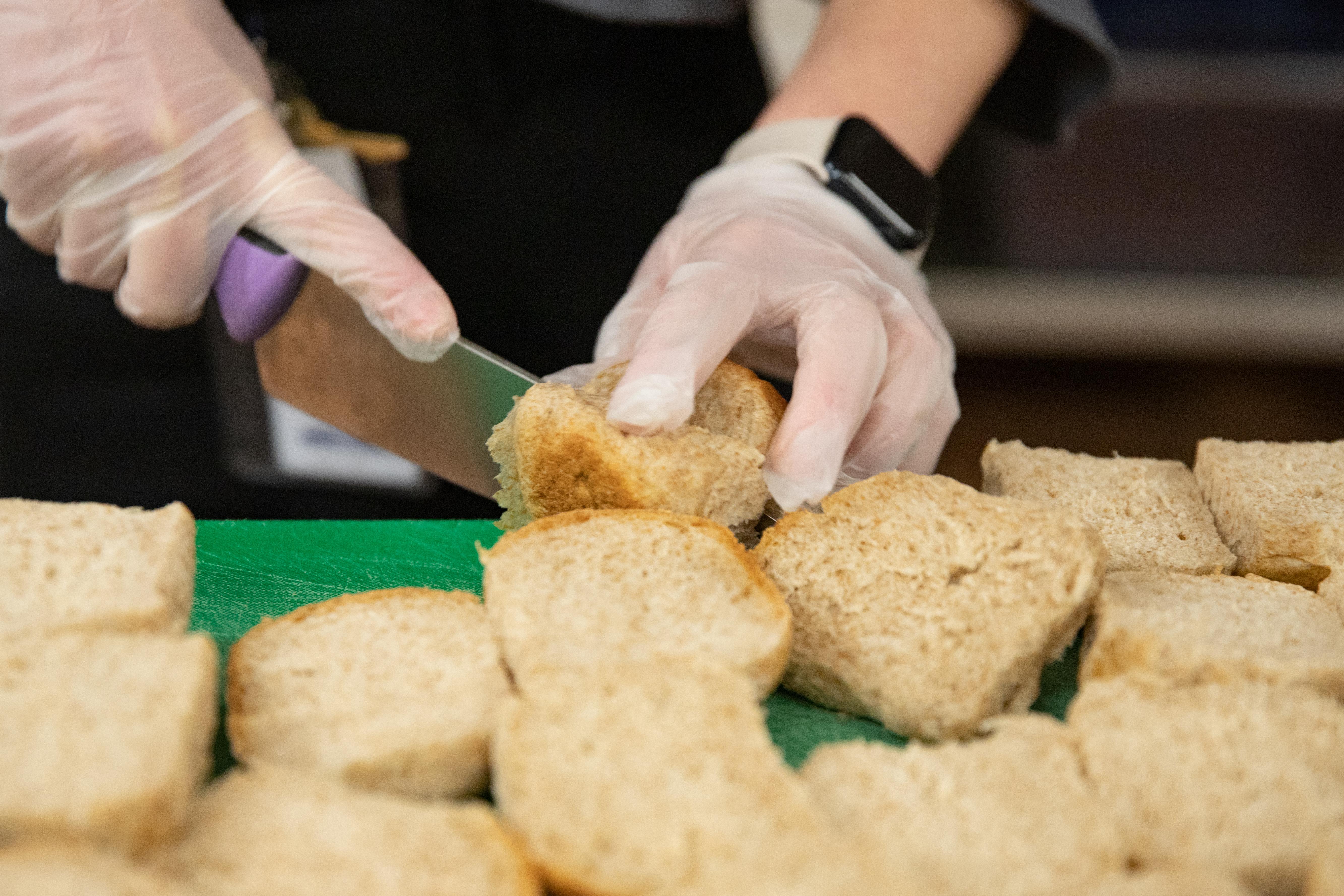 A Vermont school nutrition specialist slices local rolls made with local grains on a green cutting board.