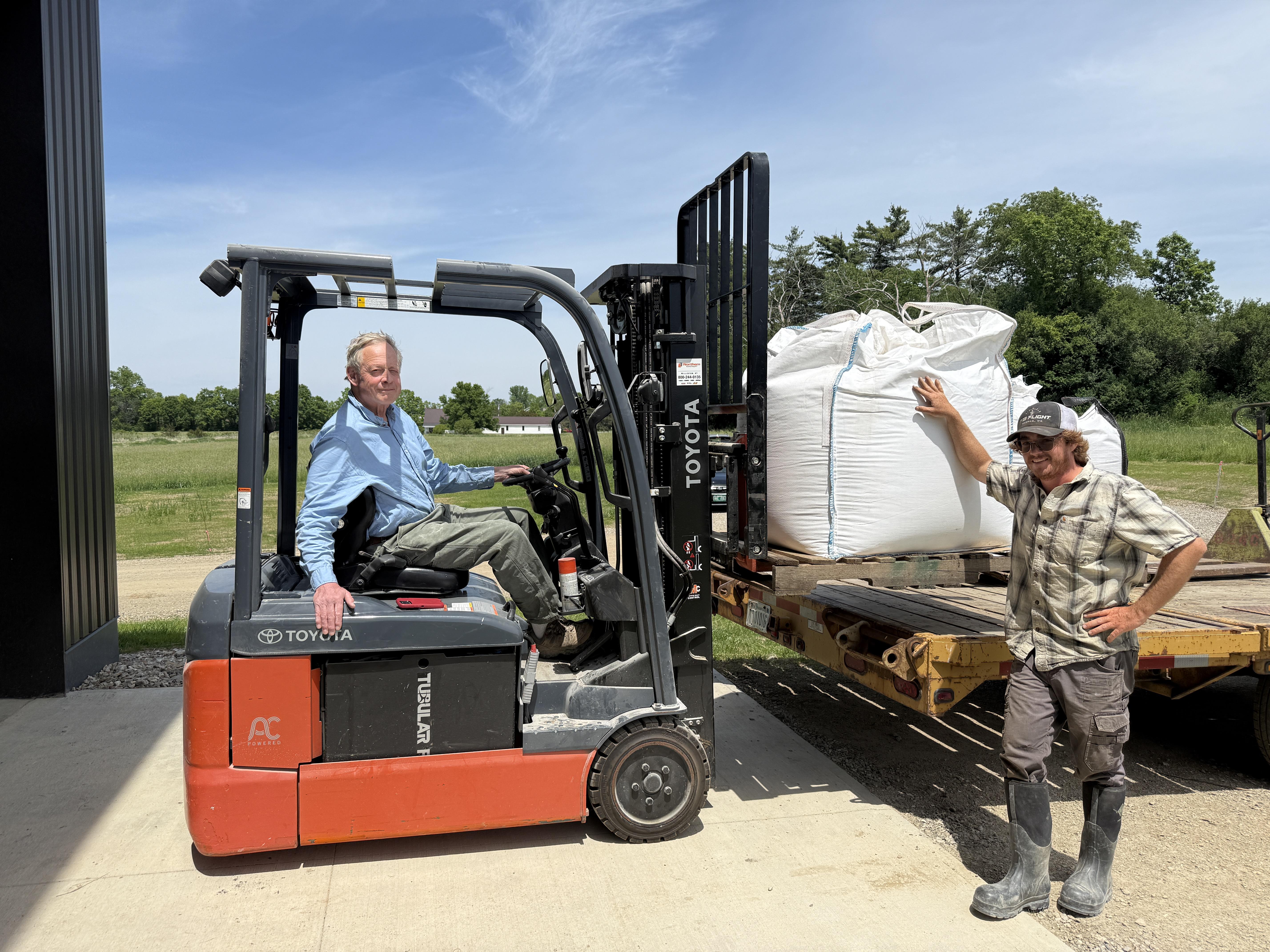 Todd Hardie of the Champlain Valley Grain Center is seen seated on a forklift receiving a load of fresh grain from Tyler of Granite Grains