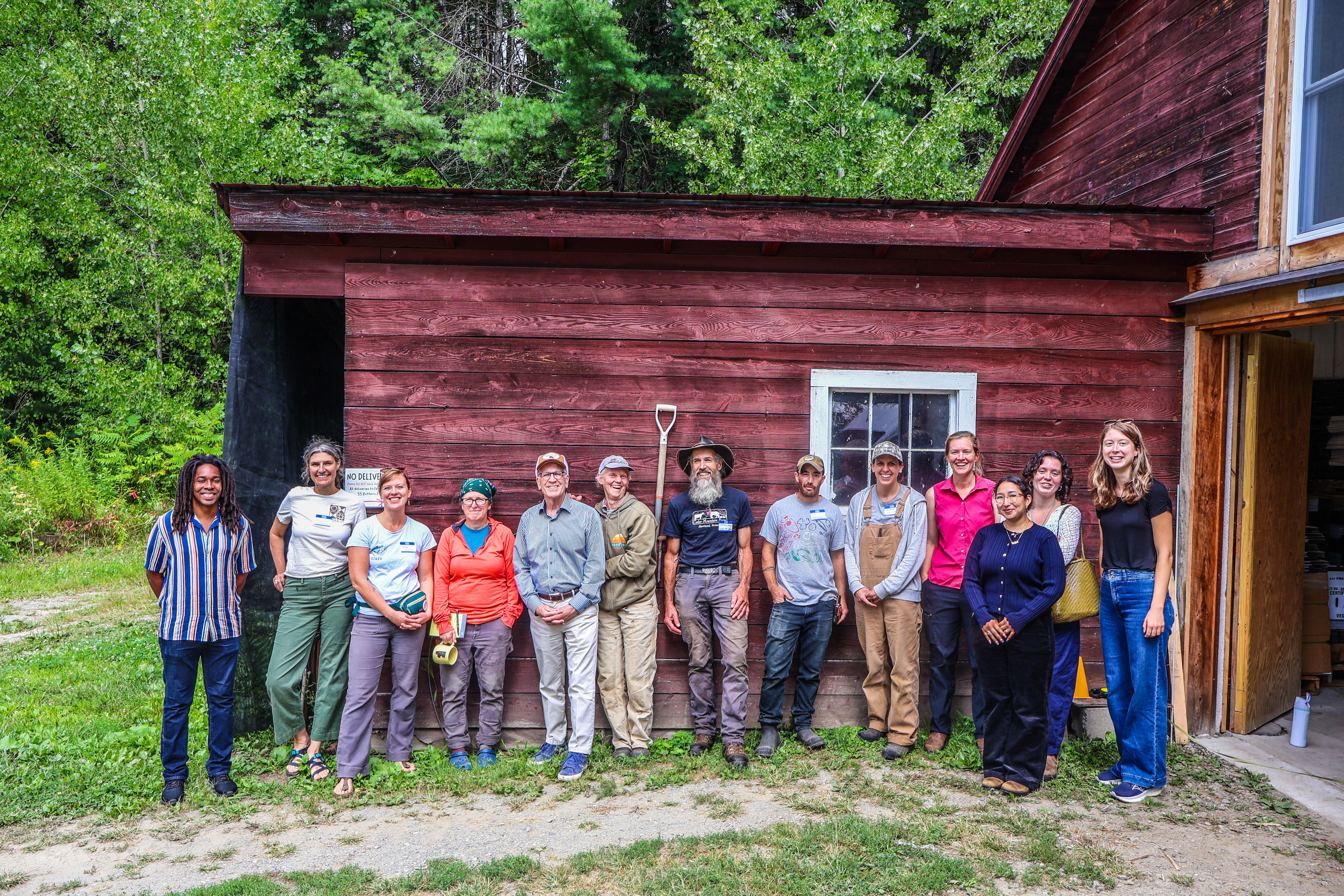 Vermont farmers lined up along the side of a red barn at Honey Field Farm with Senator Peter Welch and his staff, along with staff from NOFA-VT's policy & organizing team 