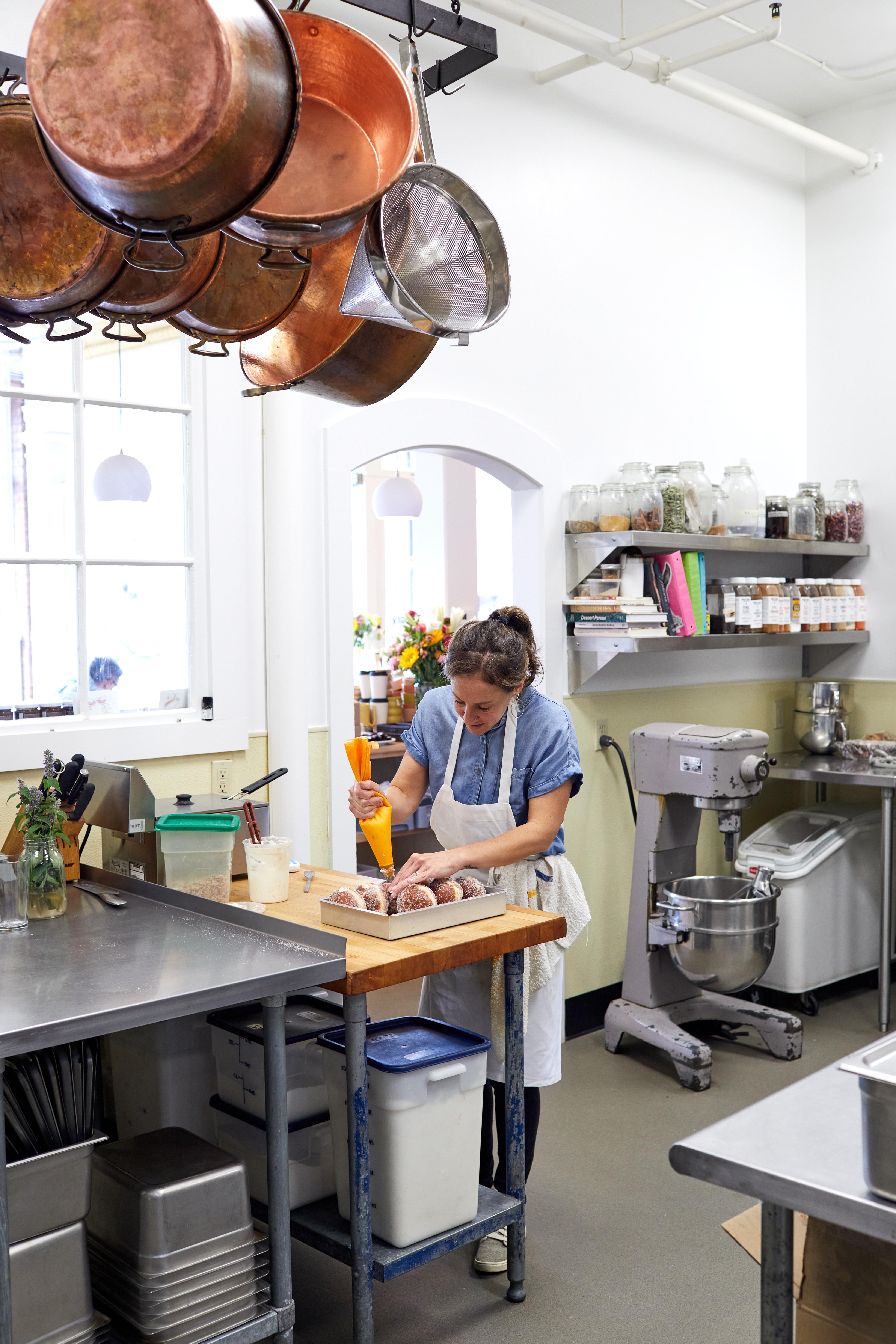 Copper jam pans hanging over work tables at Minifactory as a baker fills donuts 