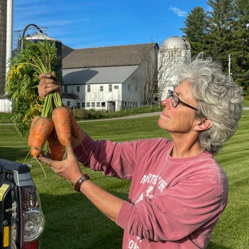 Maria, a farmer, holds up a clump of carrots, admiring them.