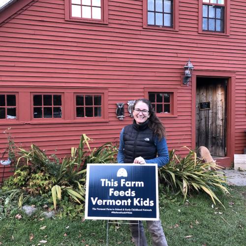 Misse stands outside with a sign that reads "this farm feeds VT kids"