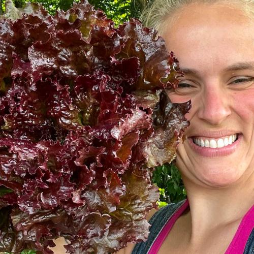 Emma smiles at the camera, holding a bundle of lettuce