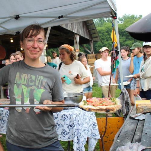 A person serves pizza at an outdoor oven